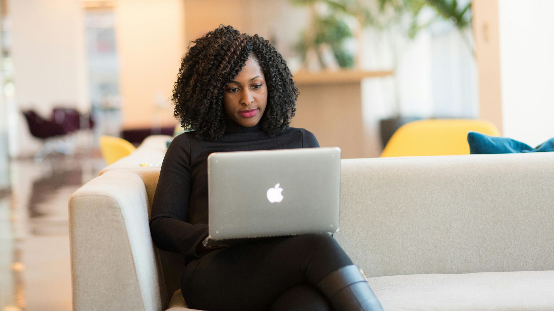 An African American woman working remotely on a laptop in a modern indoor setting.