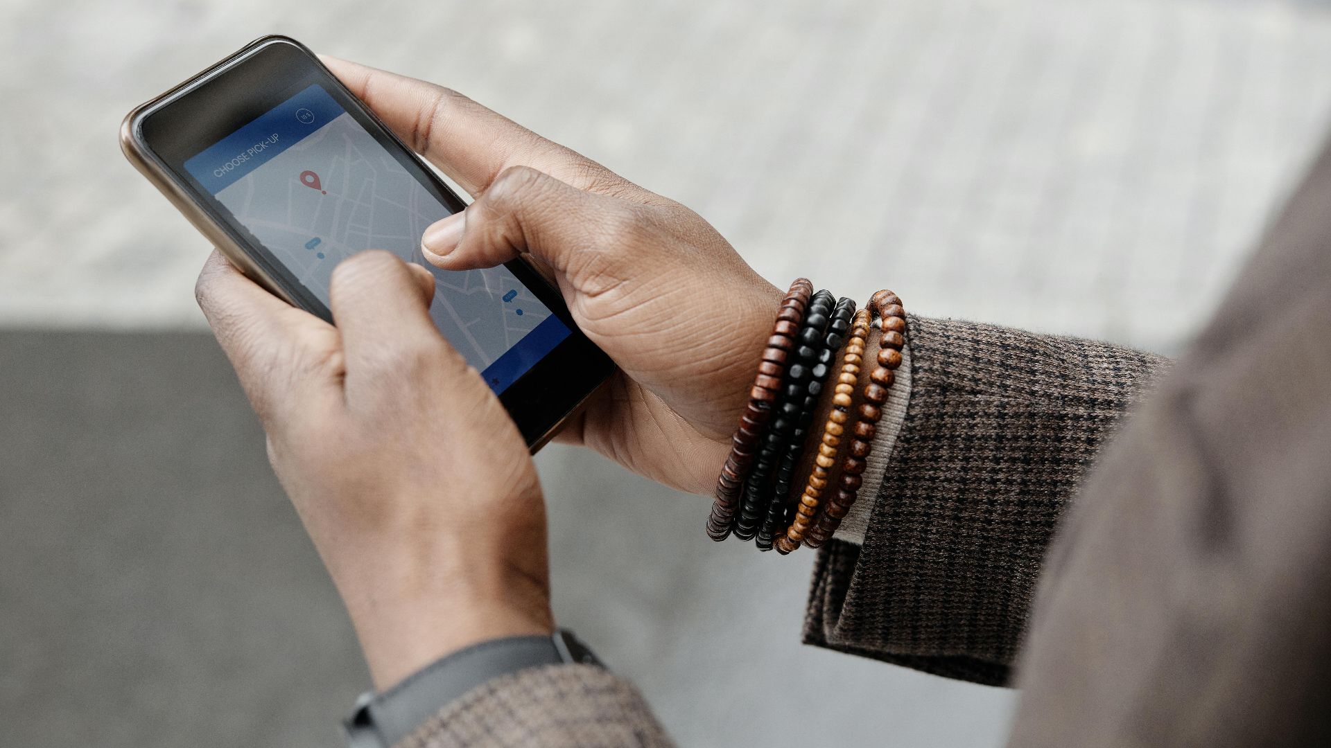 Close-up of hands with bracelets navigating on smartphone using GPS app outdoors.