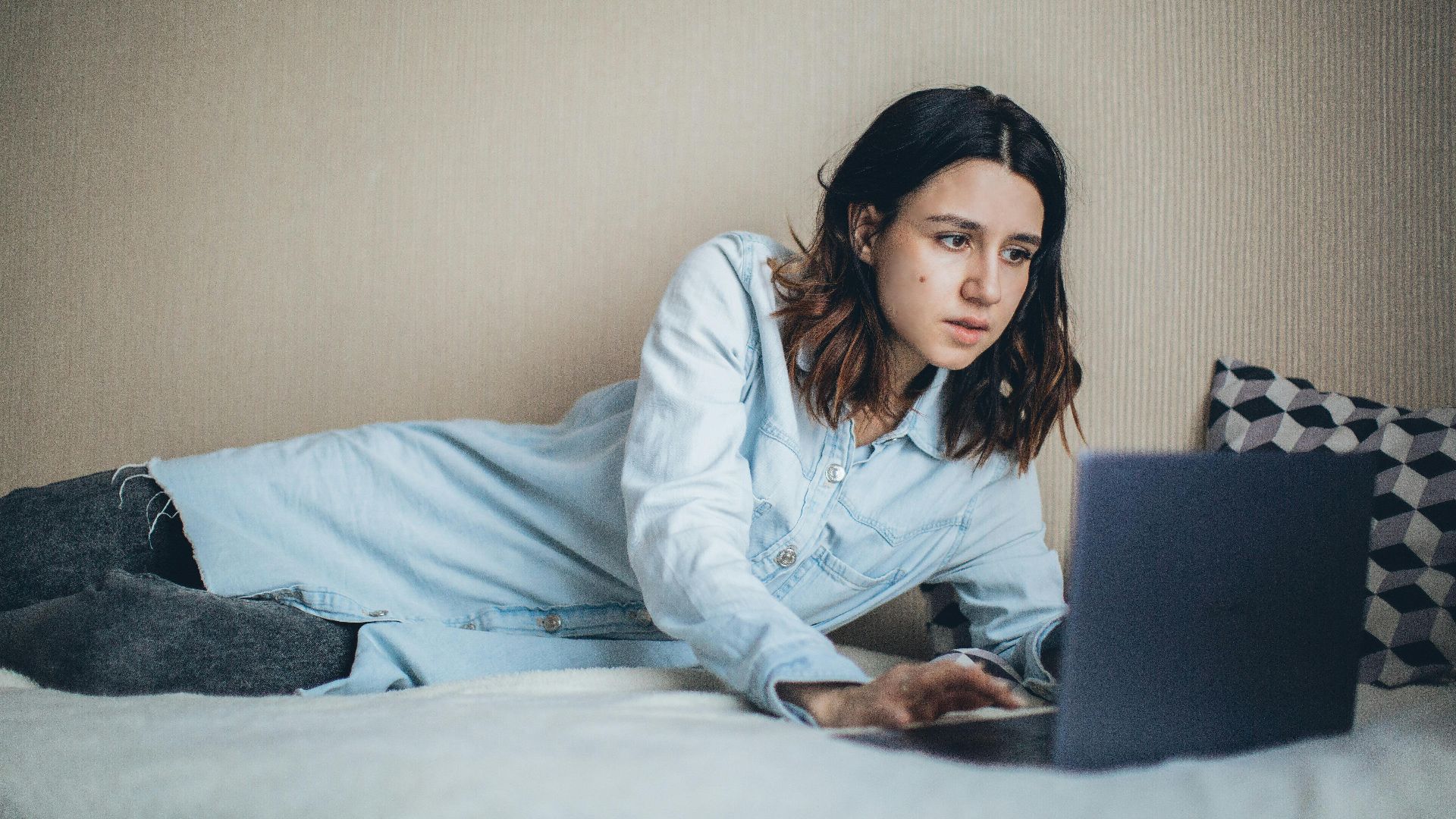 A woman relaxes in bed while working on a laptop, embodying freelance lifestyle and remote work convenience.