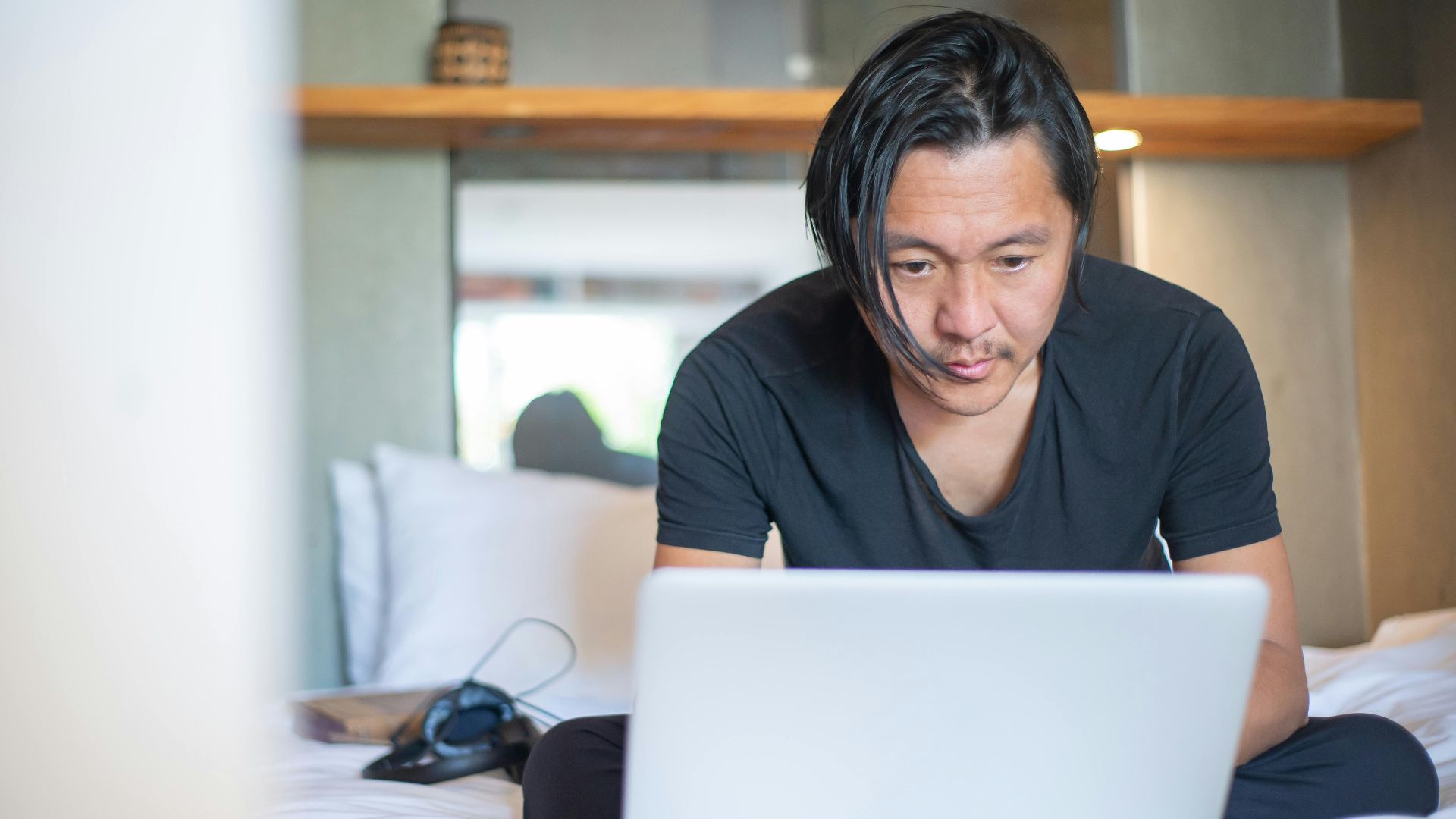 An Asian man working from home on a laptop, focusing on his digital tasks in a cozy indoor setting.