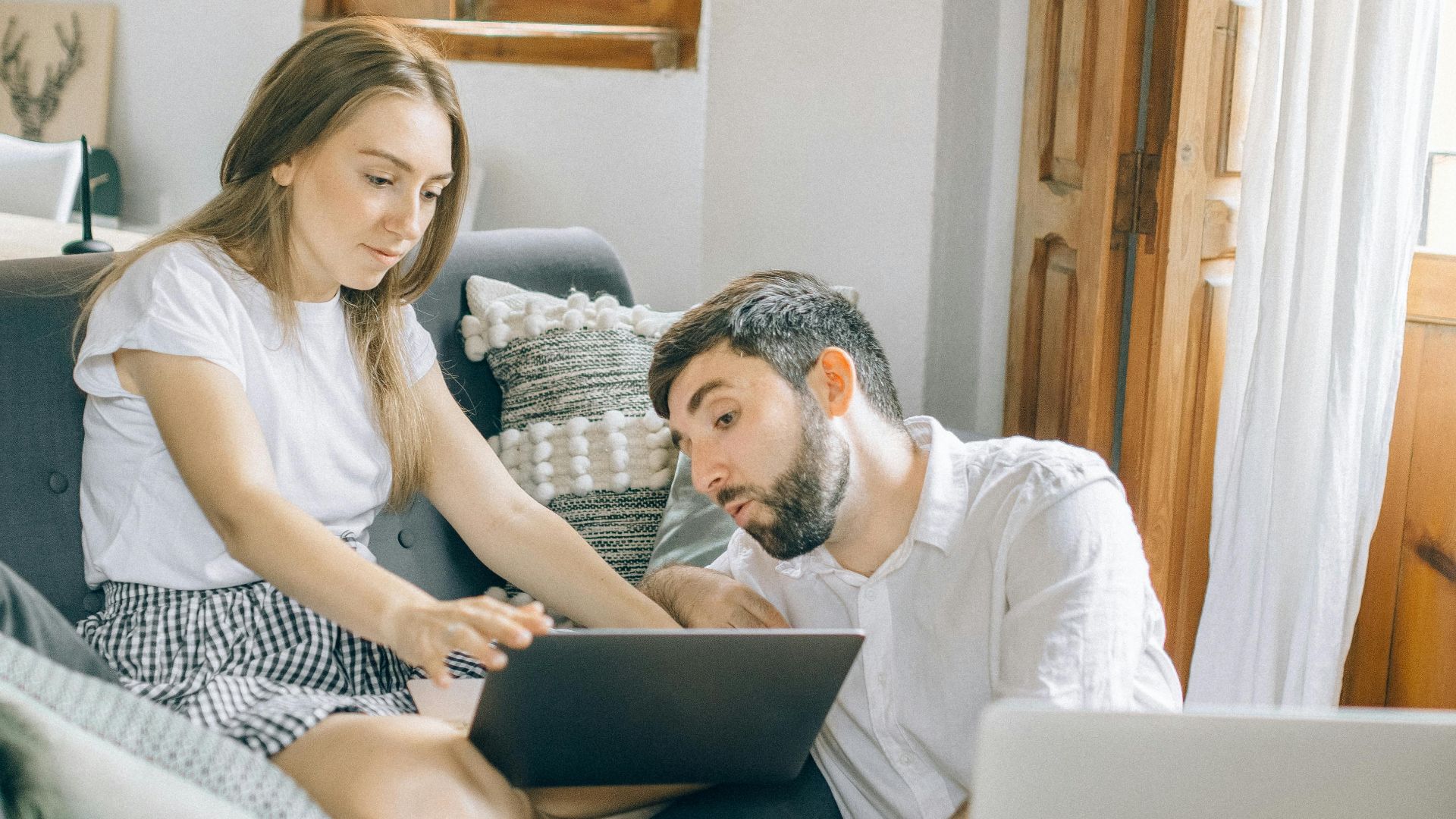 A young couple working together on laptops in a cozy living room setting, representing remote work.