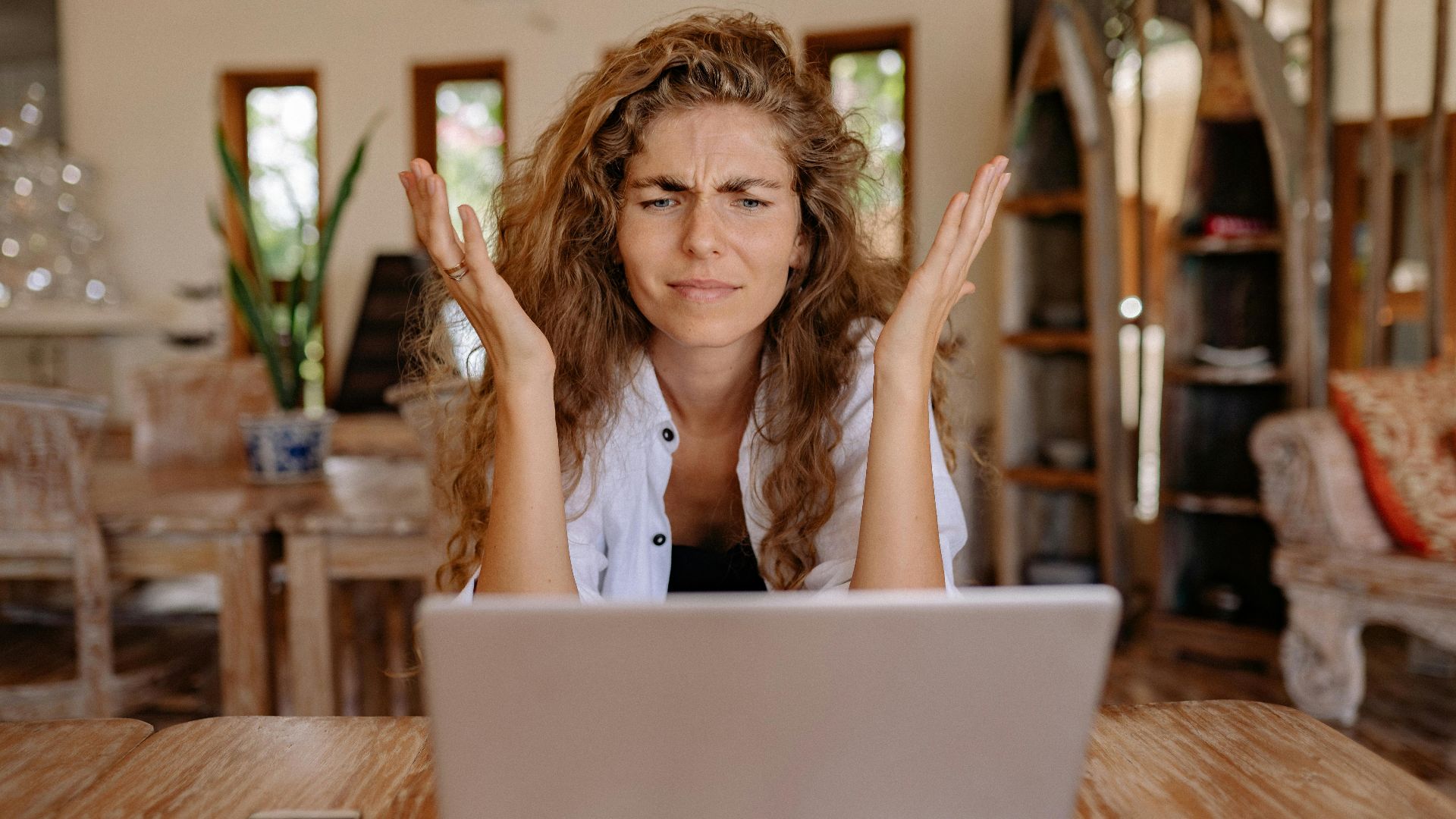 A woman frustrated with her laptop while working remotely indoors, expressing stress.