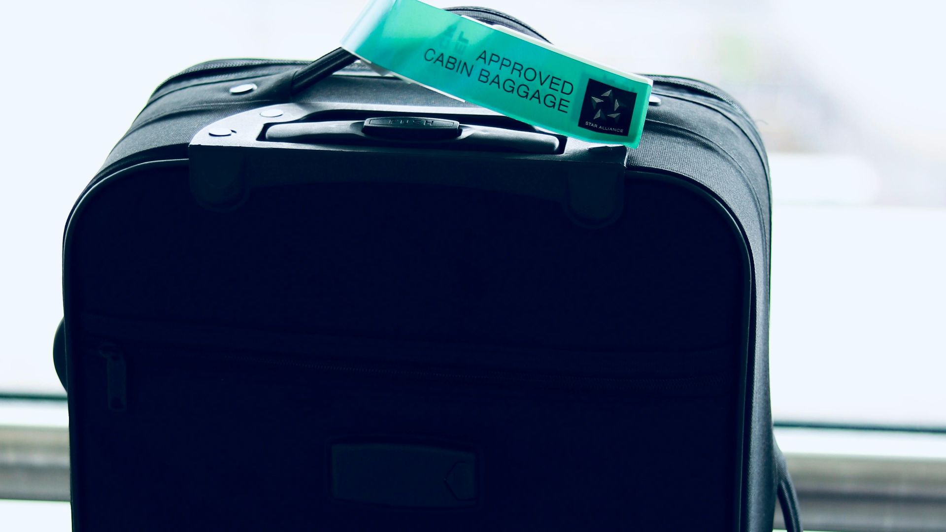 Close-up of a black suitcase with a cabin approved tag in airport setting.