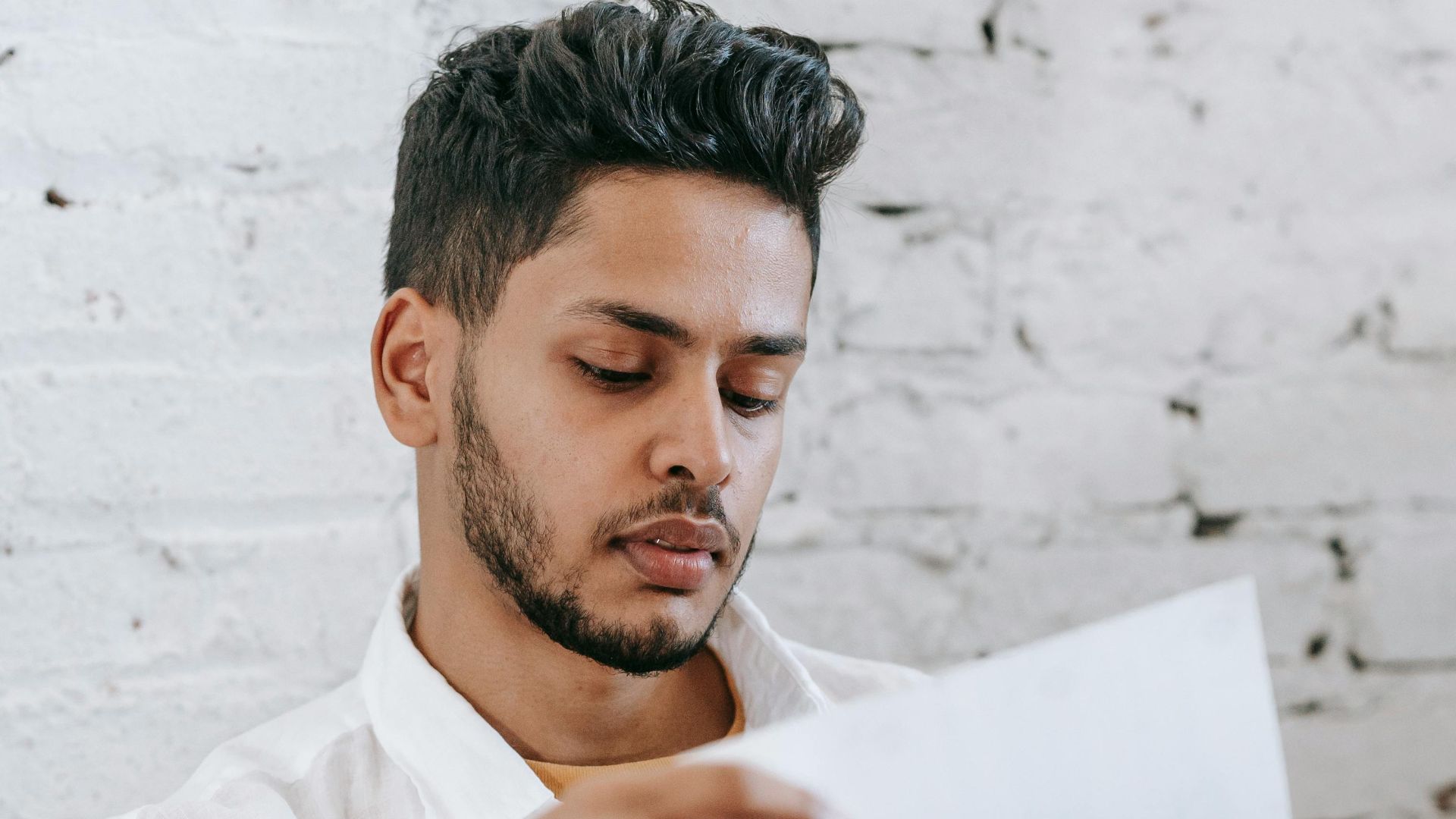 Young man attentively reviewing financial documents at home. Focused on paperwork.