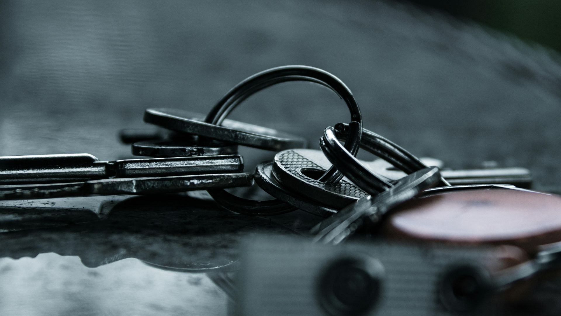 A dramatic close-up of metal keys on a reflective surface, capturing a moody and conceptual still life.