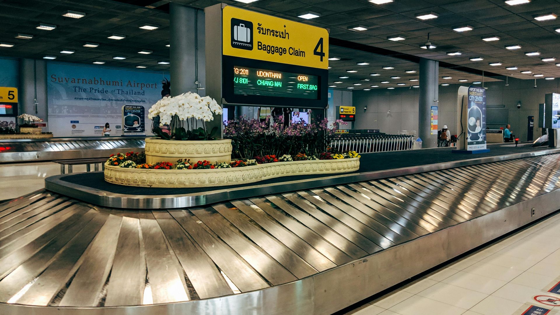 Modern baggage claim area at Suvarnabhumi Airport in Bangkok with luggage carousel and signage.