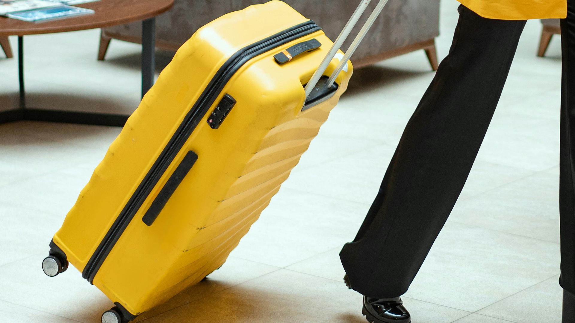 Stylish woman walking in hotel lobby pulling a bright yellow suitcase.