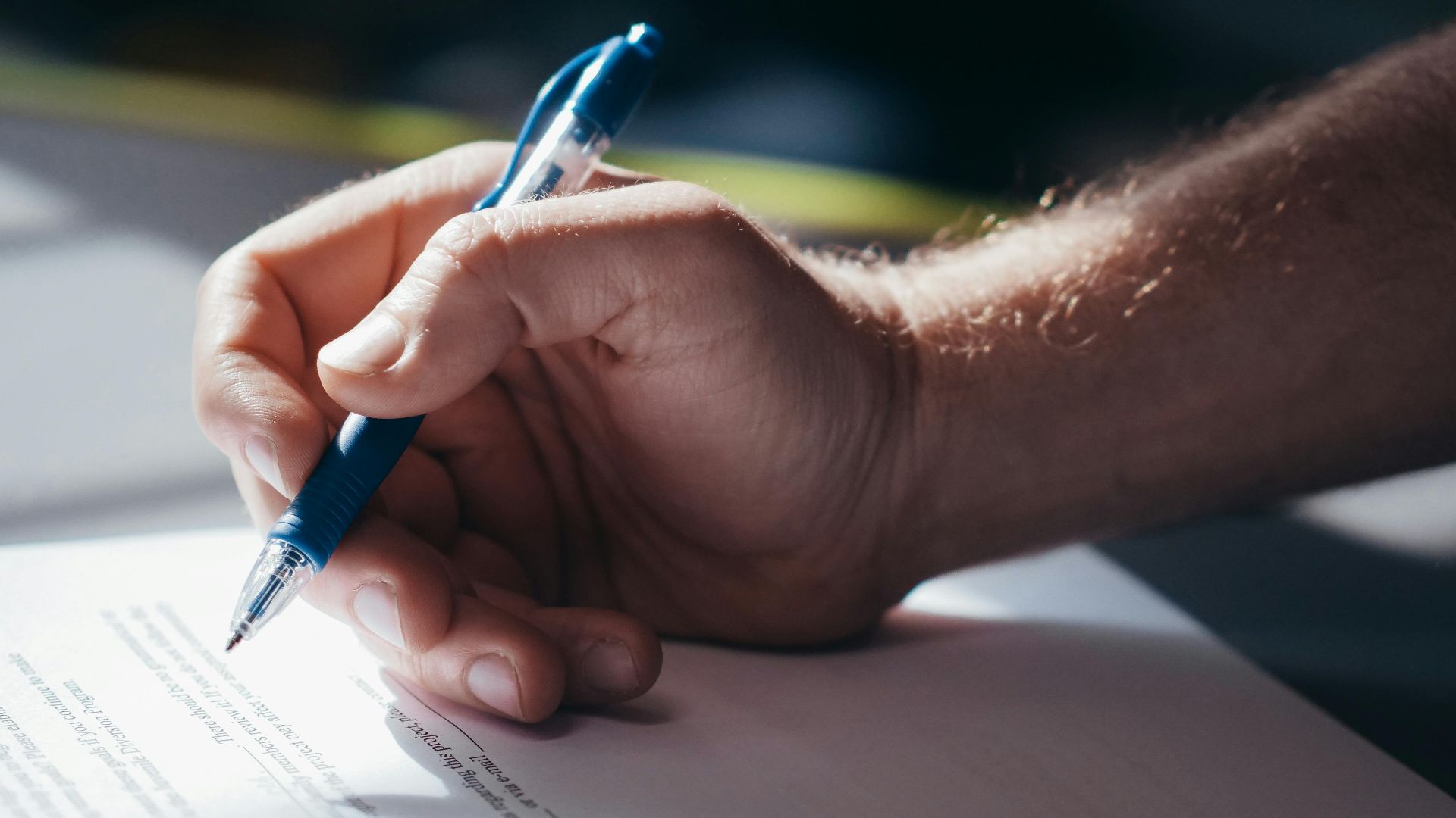 Detailed shot of a hand holding a blue pen while signing a document. Ideal for legal and business themes.