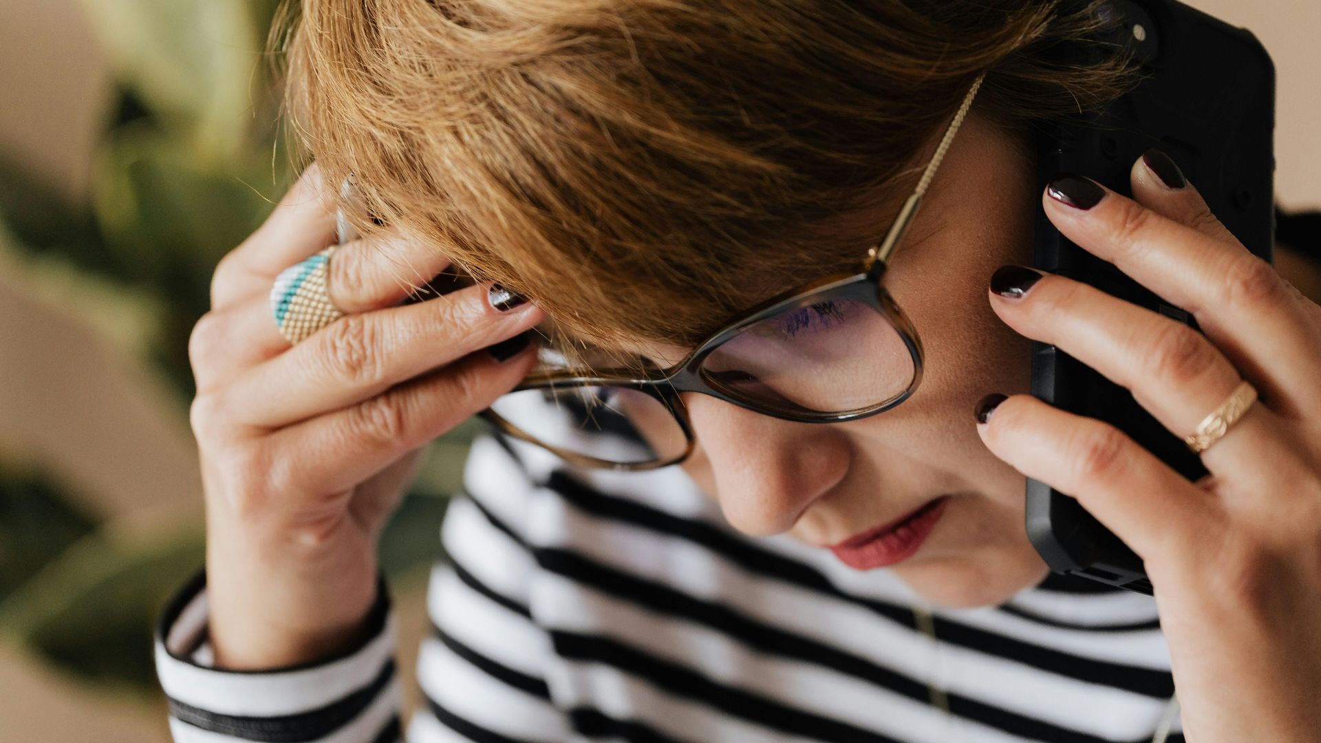 Focused woman with eyeglasses discussing work over a phone call, looking concerned and thoughtful.