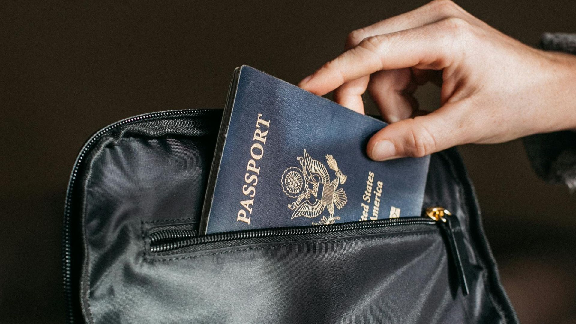 Close-up of a person placing a passport into a leather bag, ready for travel.