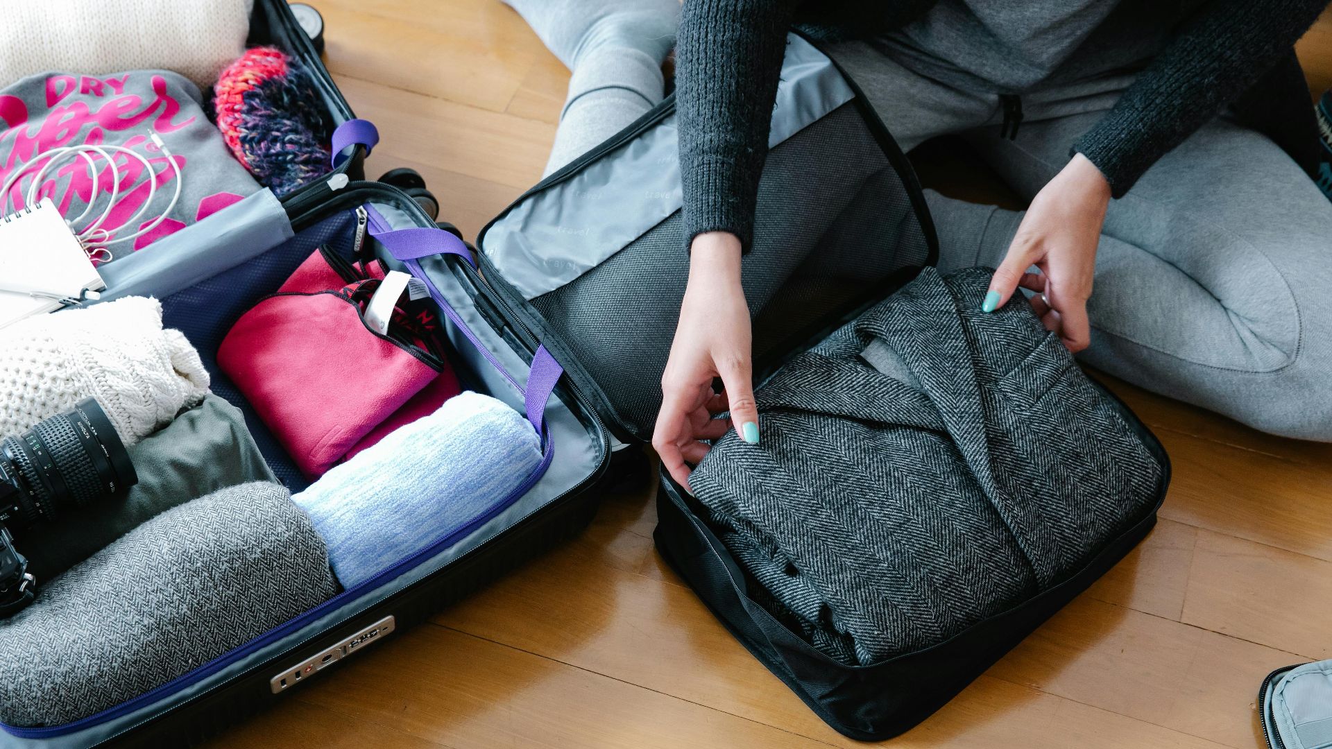 Woman organizes clothing and camera gear in a suitcase for travel.