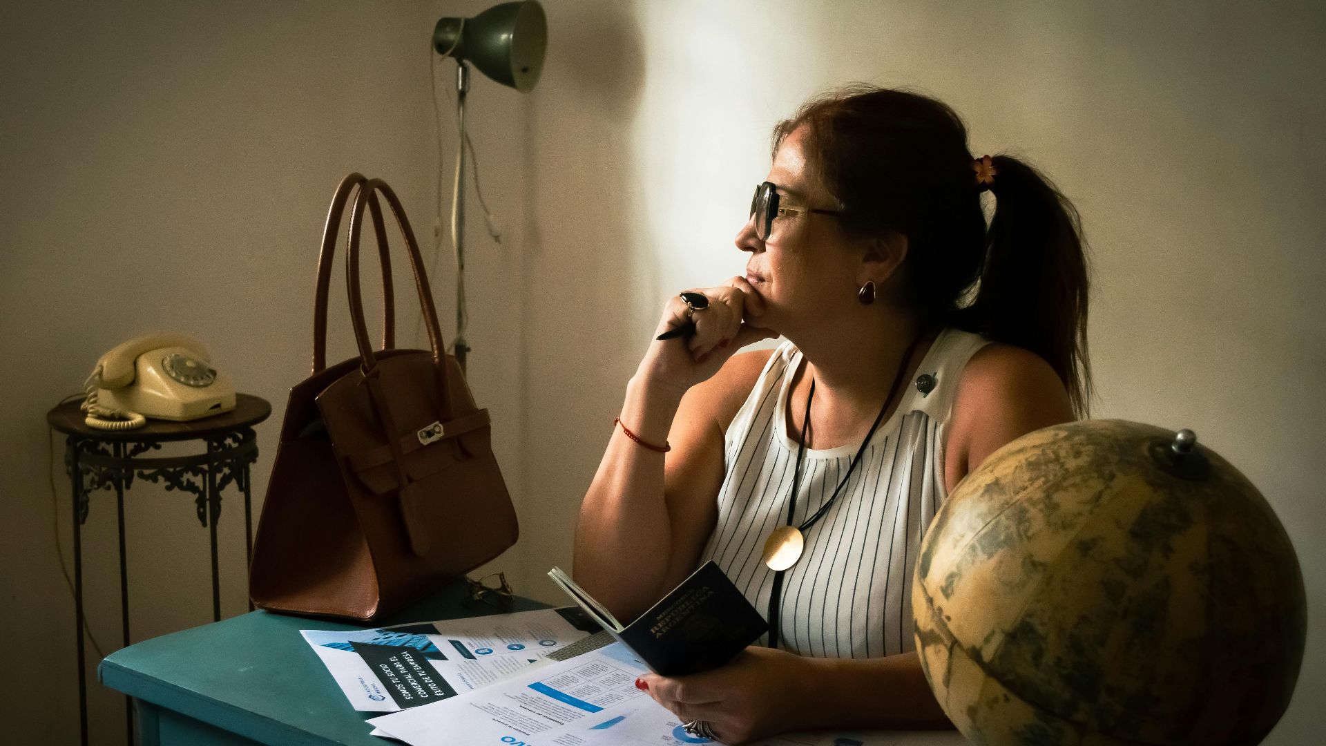 A woman in a vintage office contemplating with a globe, documents, and classic phone.