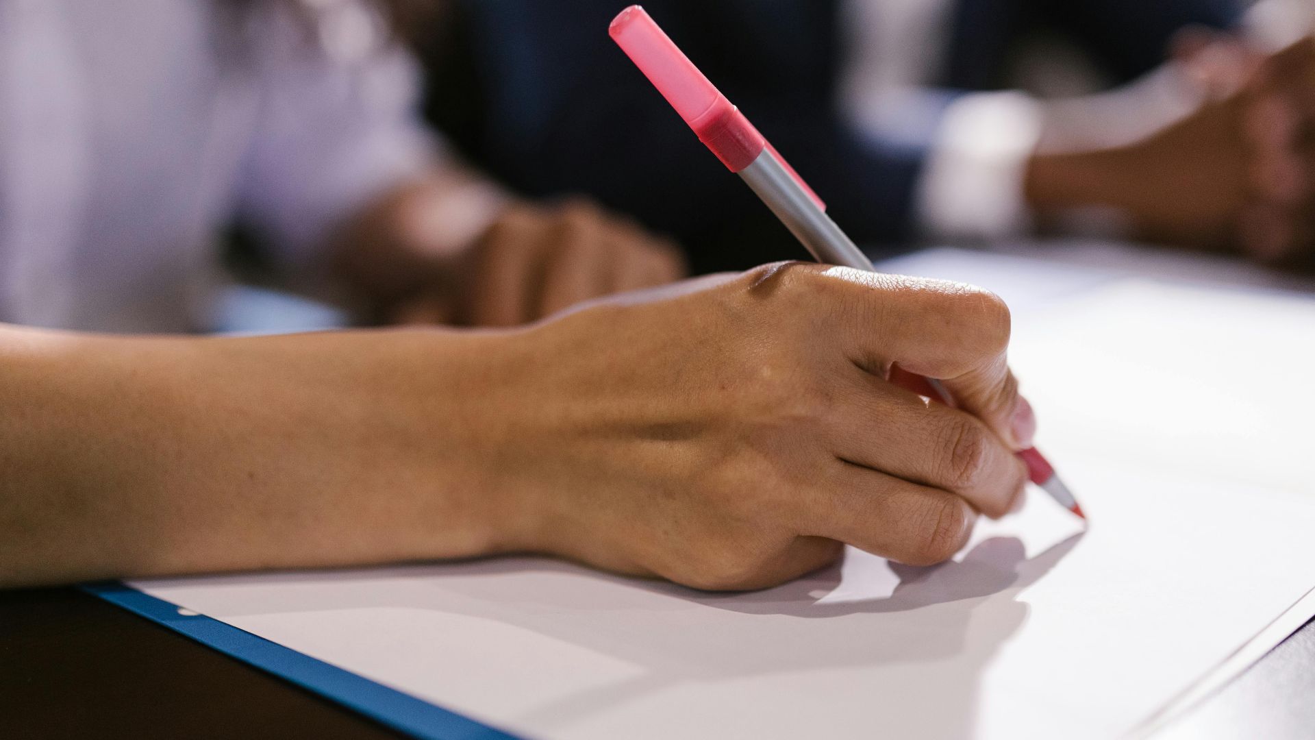 Detailed close-up of a person writing on paper with a pen in an office setting.