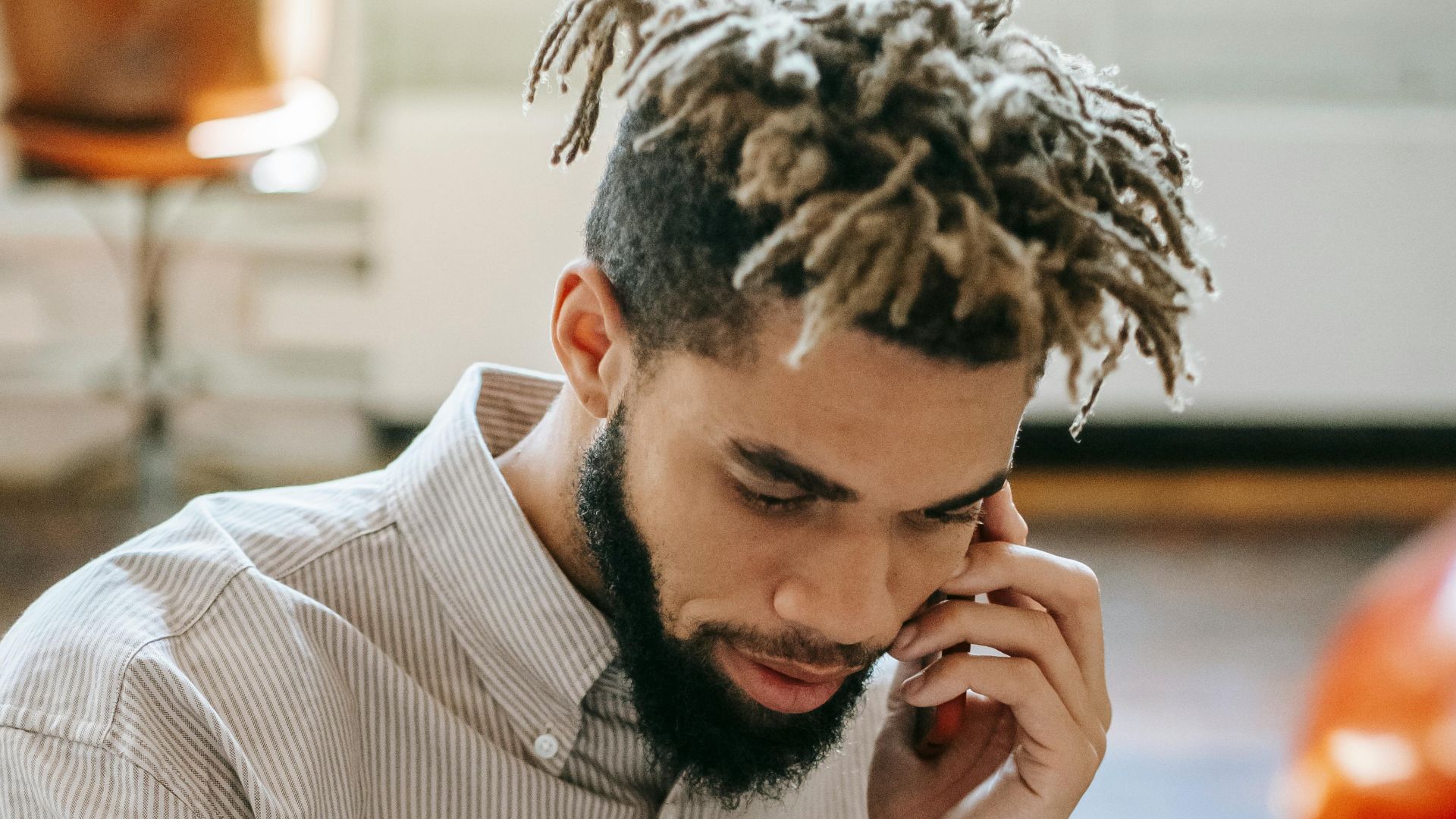 African American man multitasking, talking on phone and writing notes indoors.