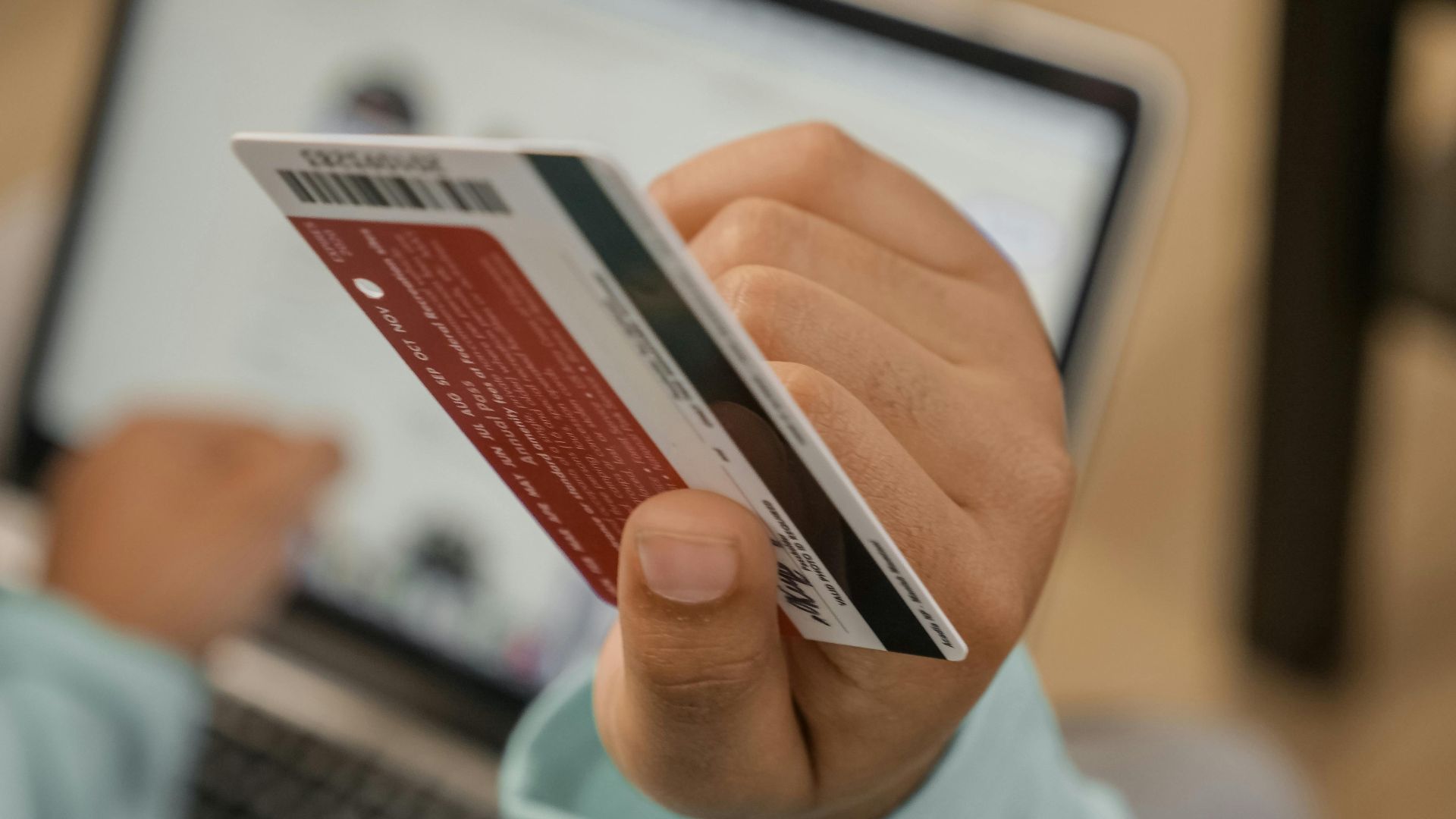 Close-up of hand holding a credit card during an online transaction on a laptop.