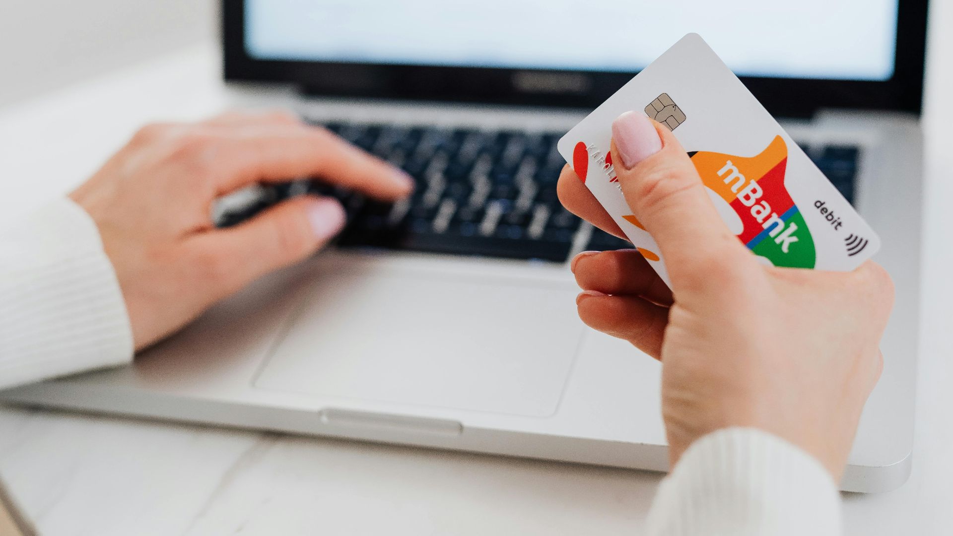 Close-up of hands using a laptop and holding a credit card for an online transaction.