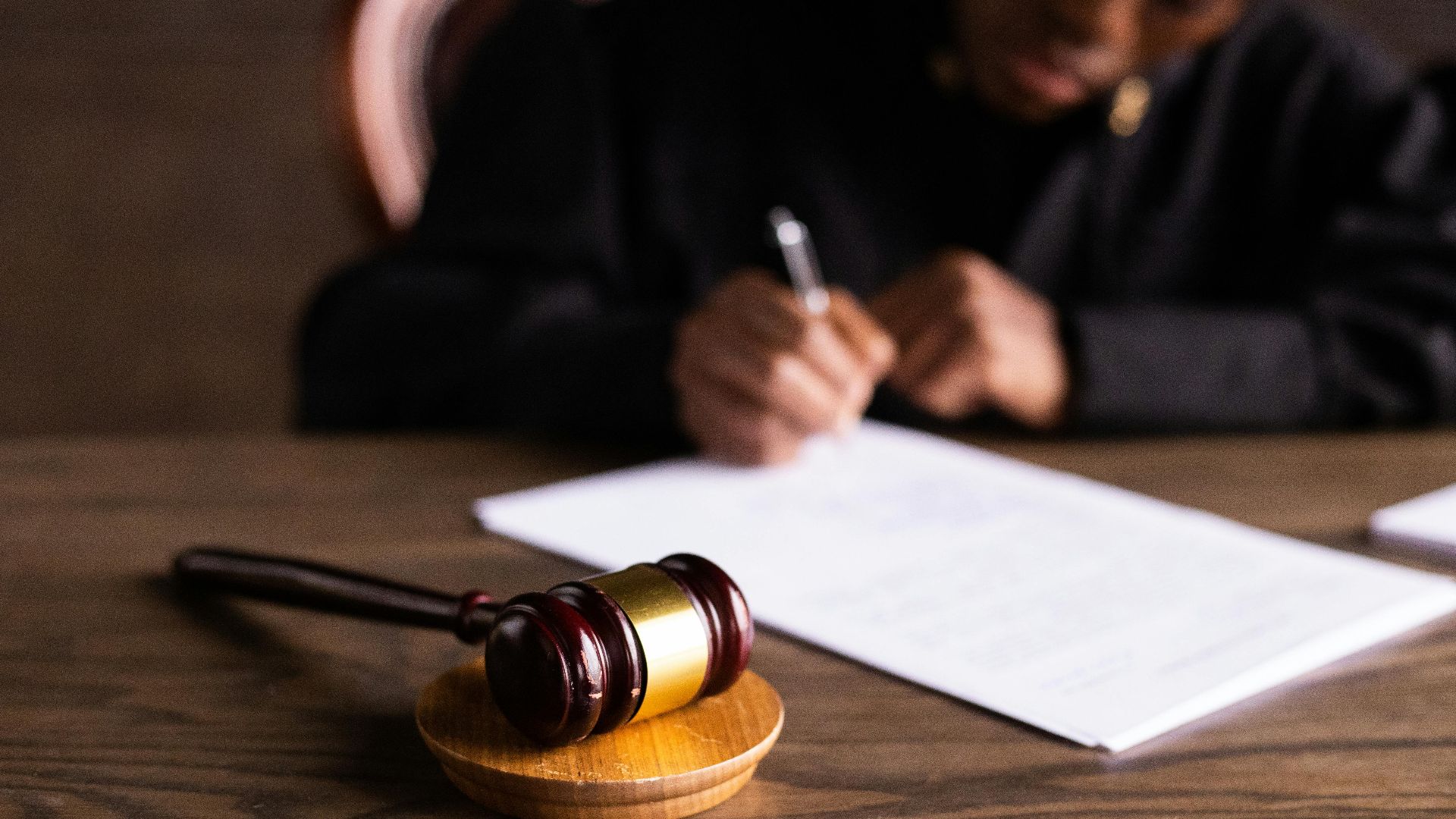 Judge signing documents at desk with focus on gavel, representing law and justice.