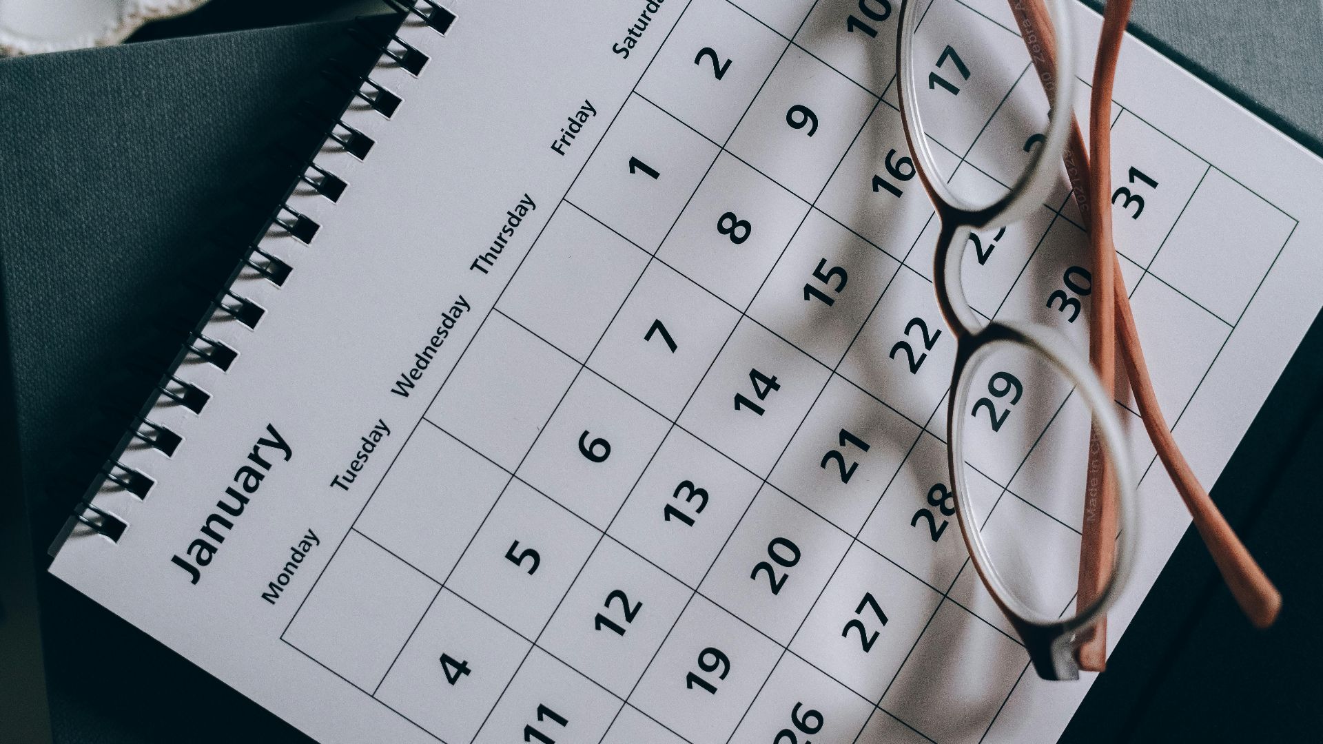 A close-up of a January calendar with eyeglasses on a table, emphasizing planning and organization.
