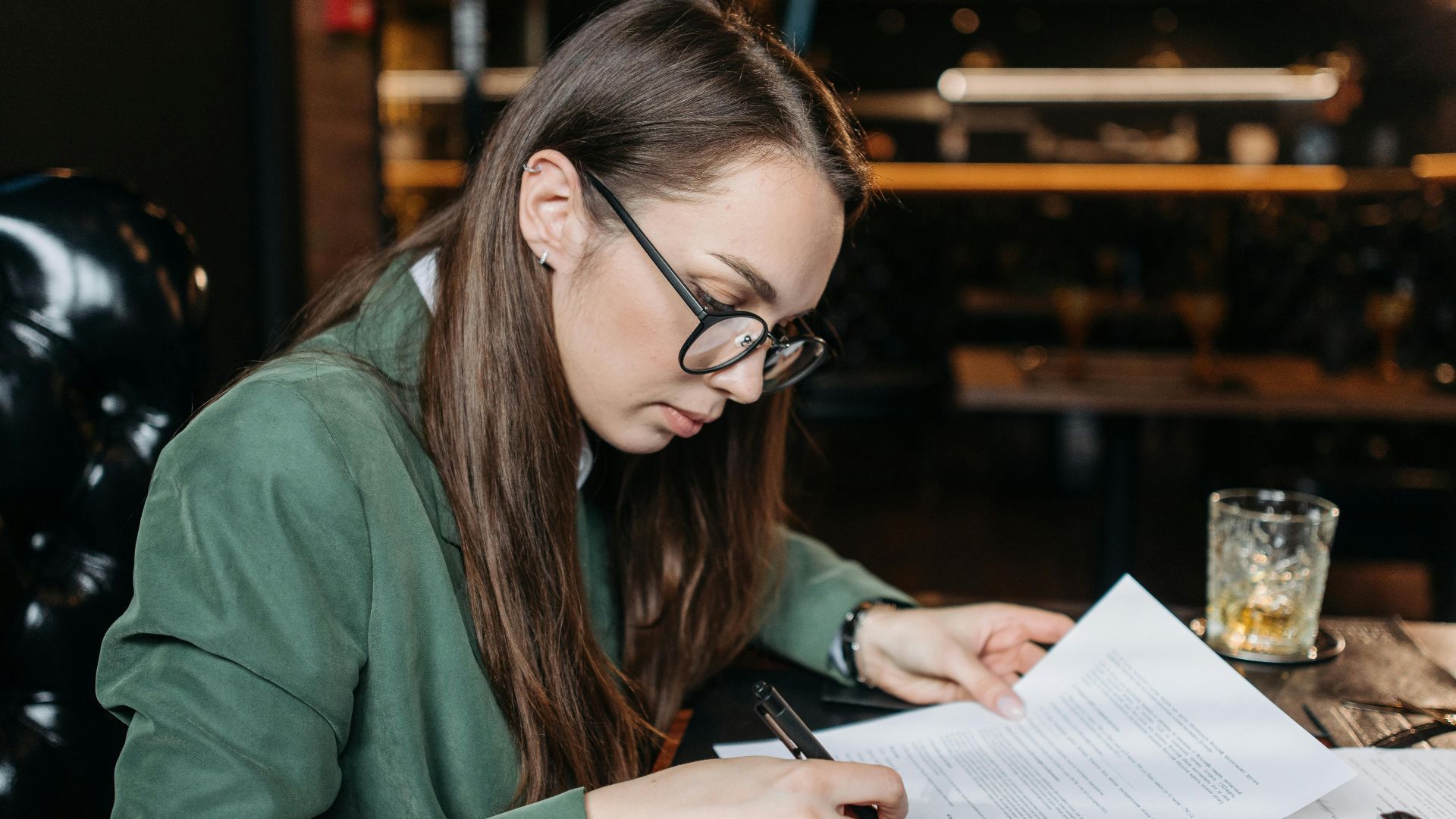 Focused businesswoman in green attire signing important documents at her desk.
