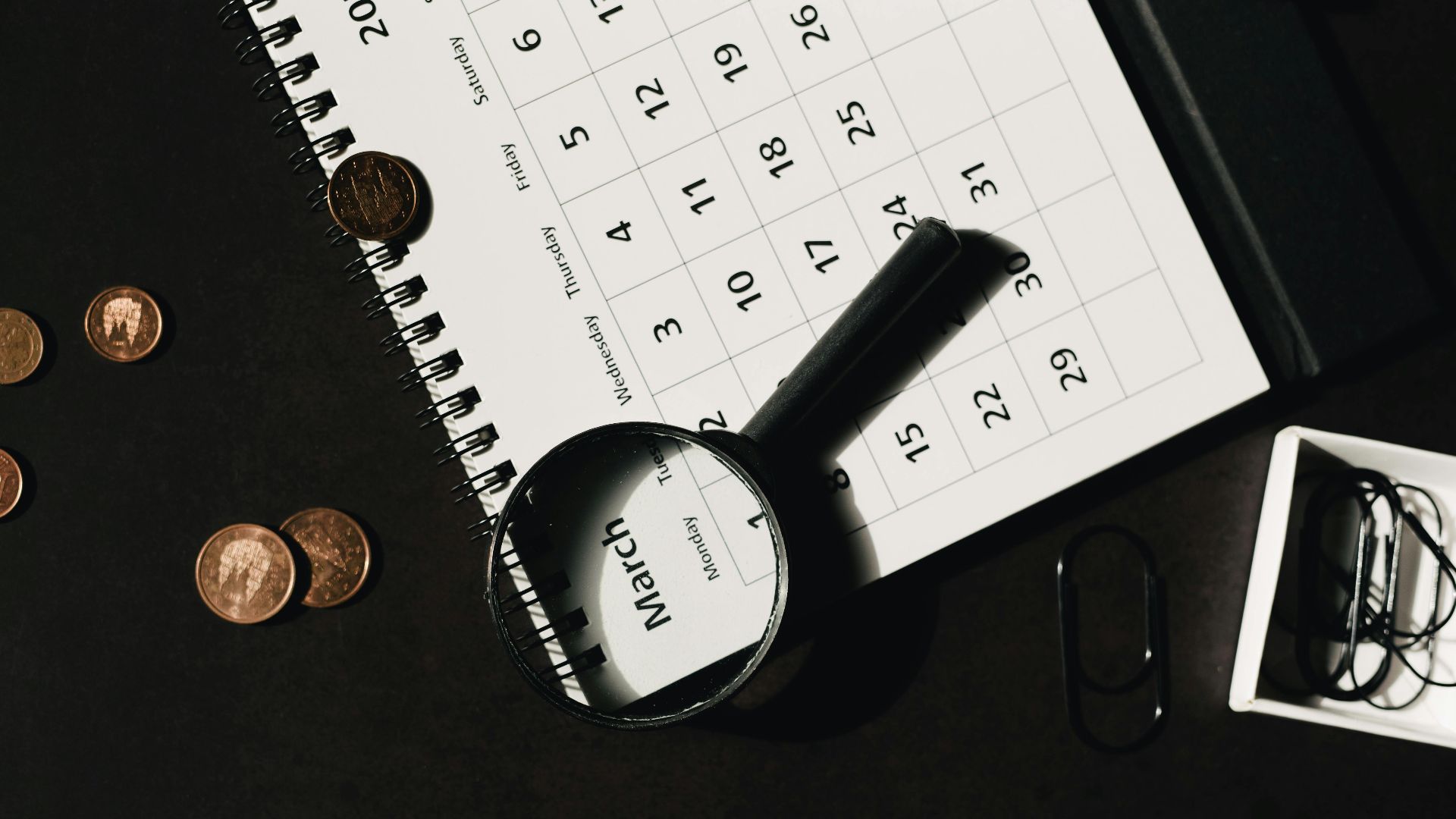 Top view of a calendar with a magnifying glass and coins, ideal for financial themes.