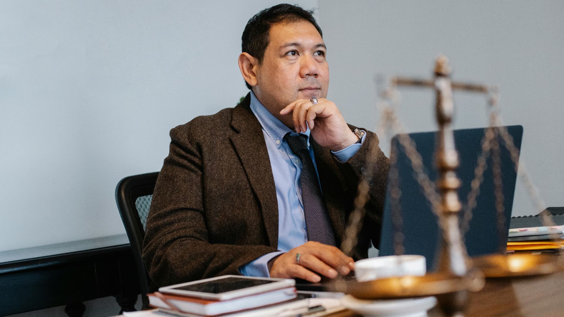 Asian lawyer at work with laptop and legal scales, focused and thoughtful.