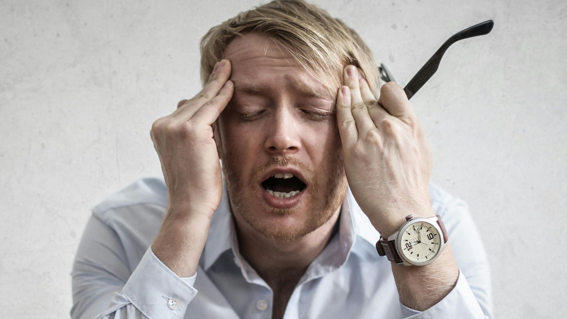 Stressed man sitting on couch, feeling overwhelmed and frustrated, expressing mental strain.