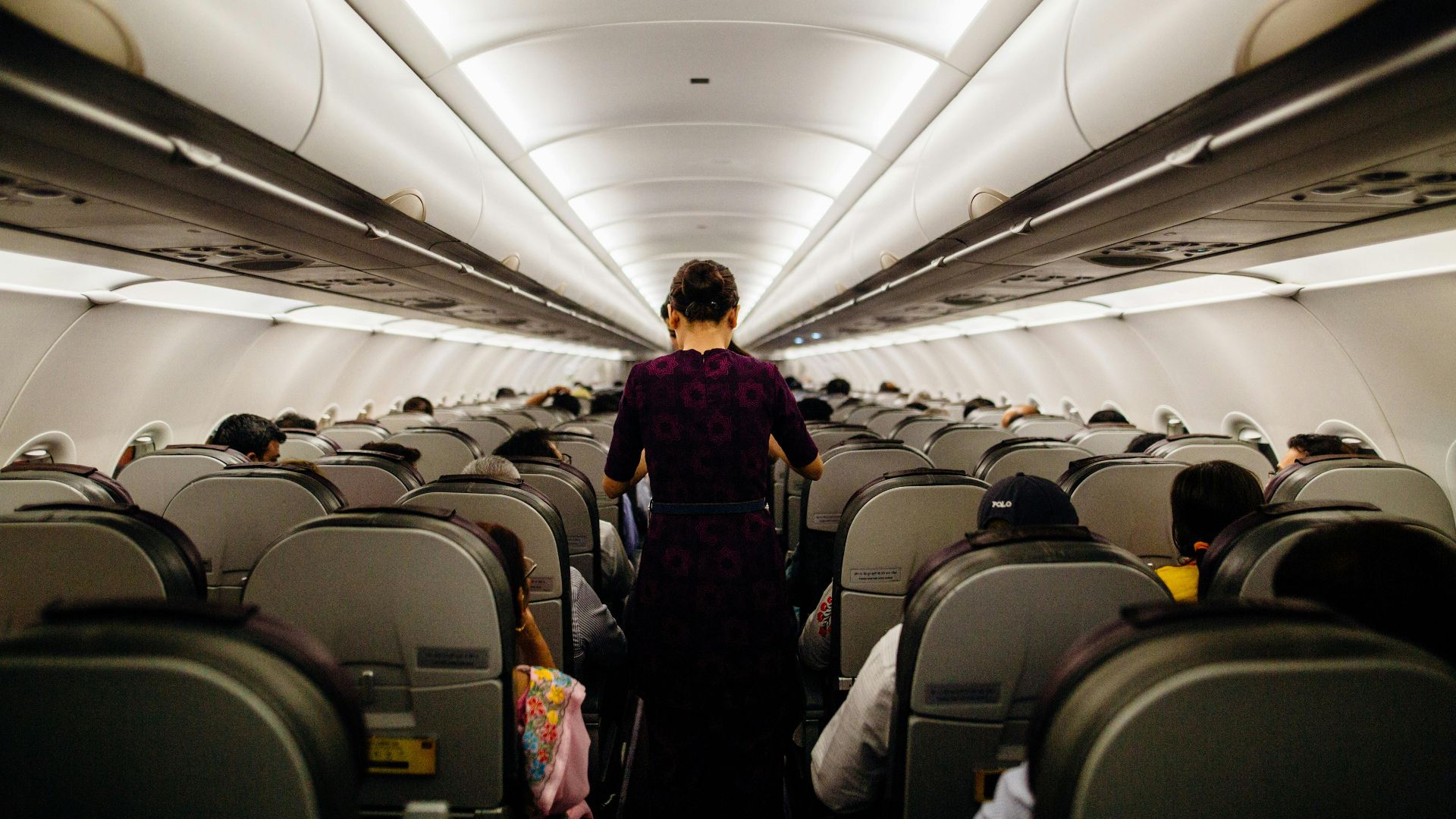 Interior view of an airplane cabin with passengers seated and a flight attendant walking down the aisle.
