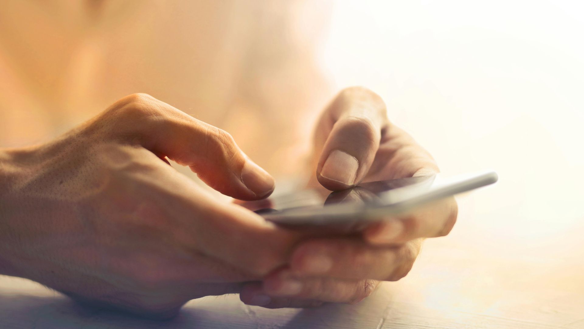 Detailed close-up of hands holding and using a smartphone indoors in soft lighting.