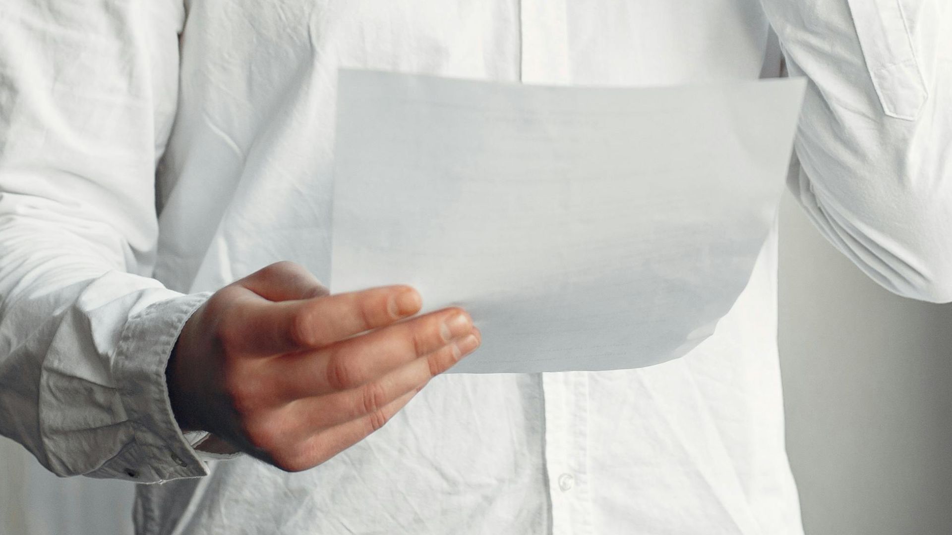 A young man in casual attire talks on the phone while holding a document indoors.