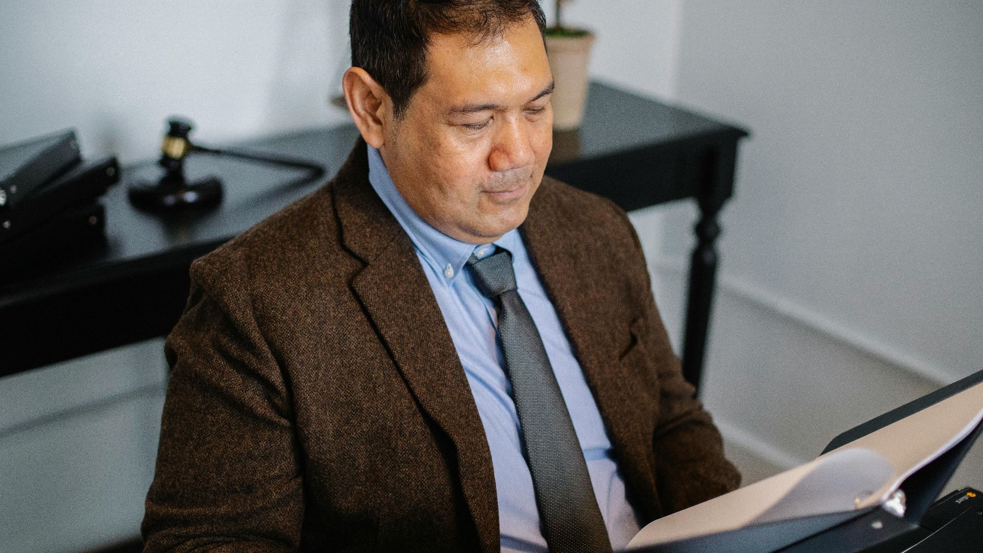 A confident Asian man in formal attire examines documents at his office desk.
