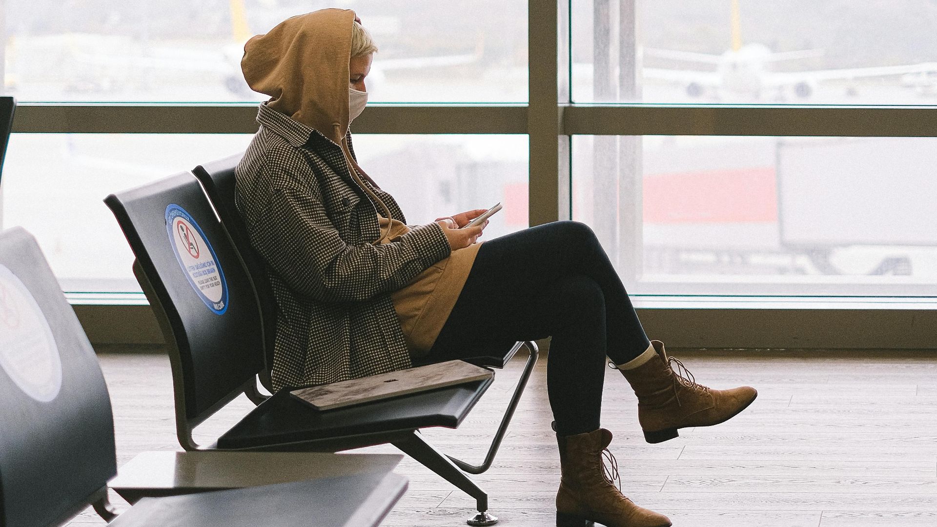 A woman with a face mask sits in an airport waiting area, adhering to safety protocols.