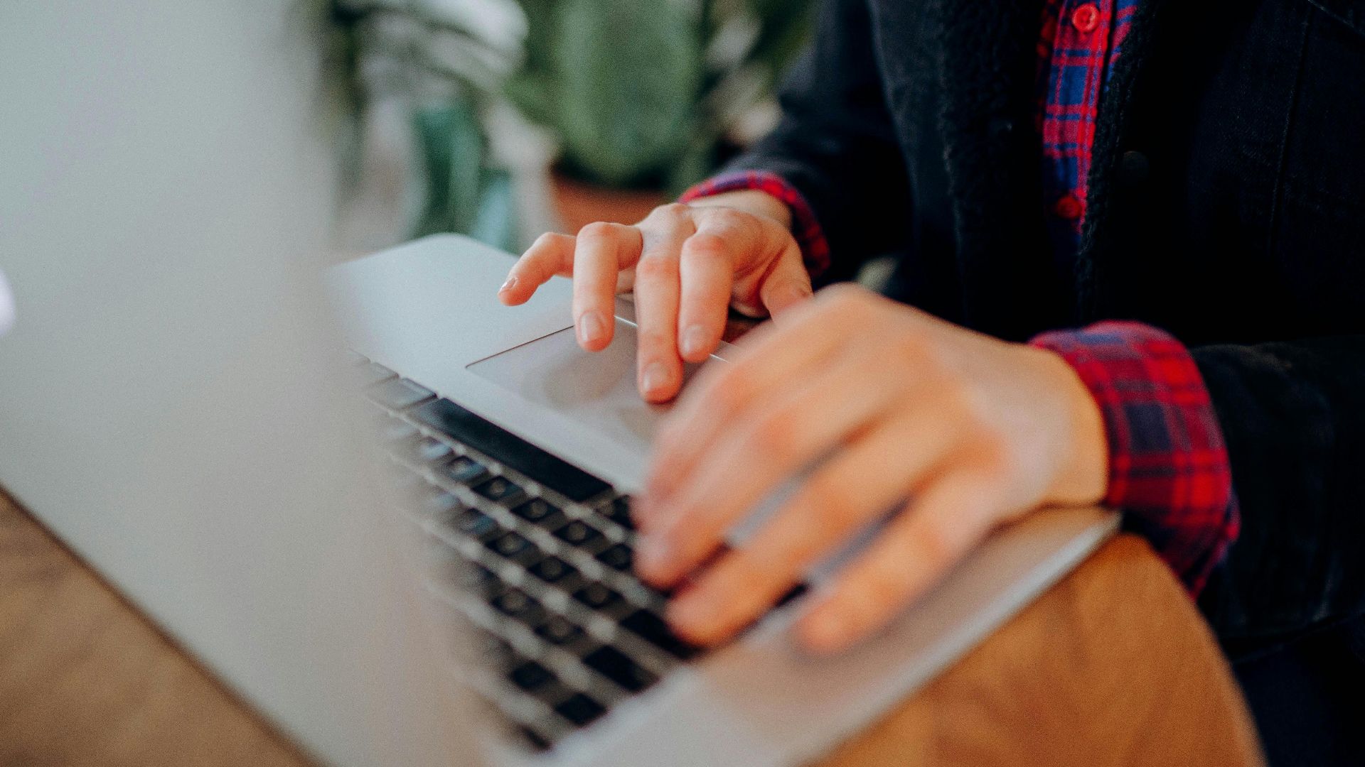 Hands typing on a laptop keyboard, close-up view, in a casual indoor setting.
