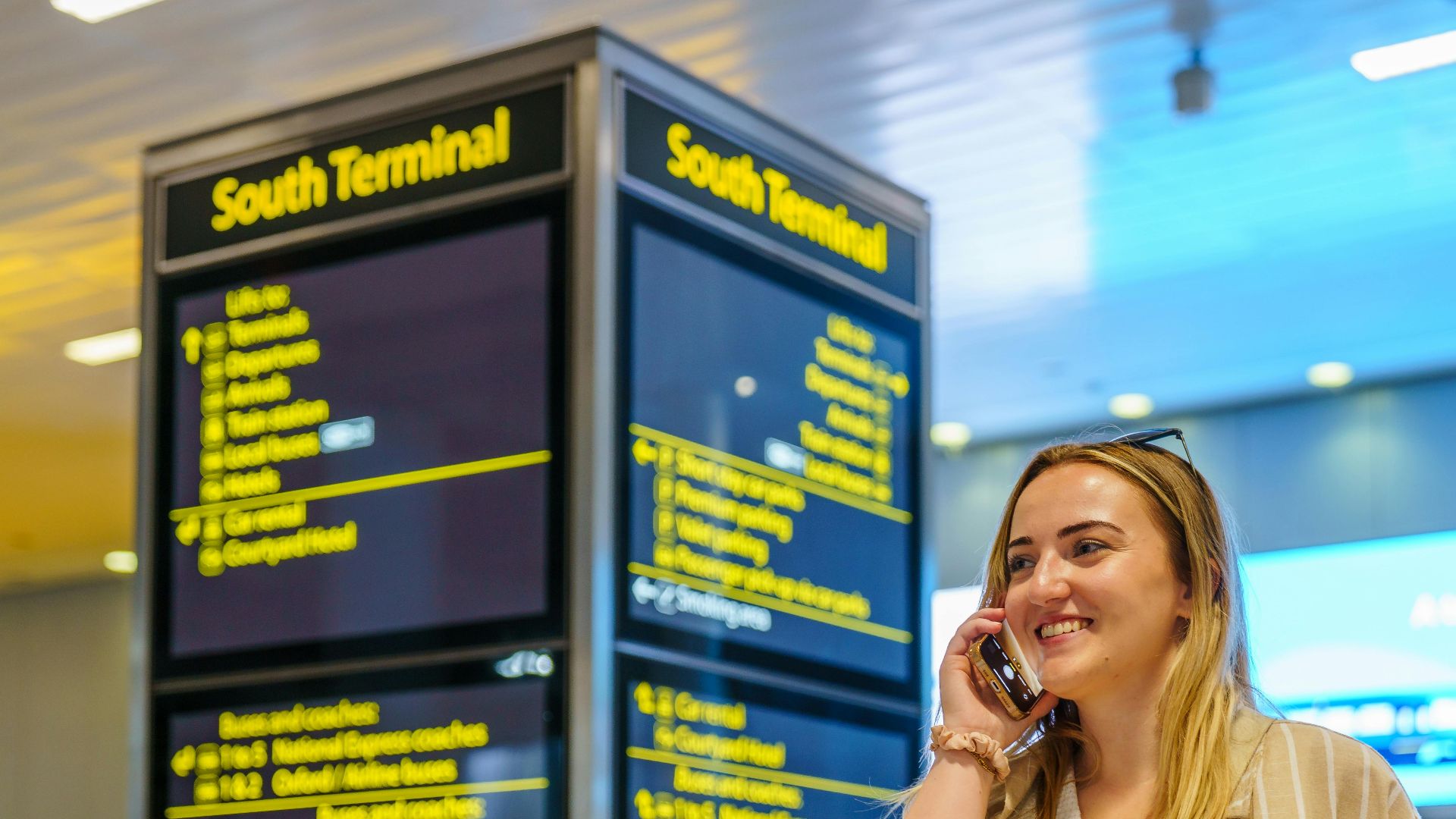 Smiling woman on phone in South Terminal of Gatwick Airport, Horley, enjoying her travel experience.