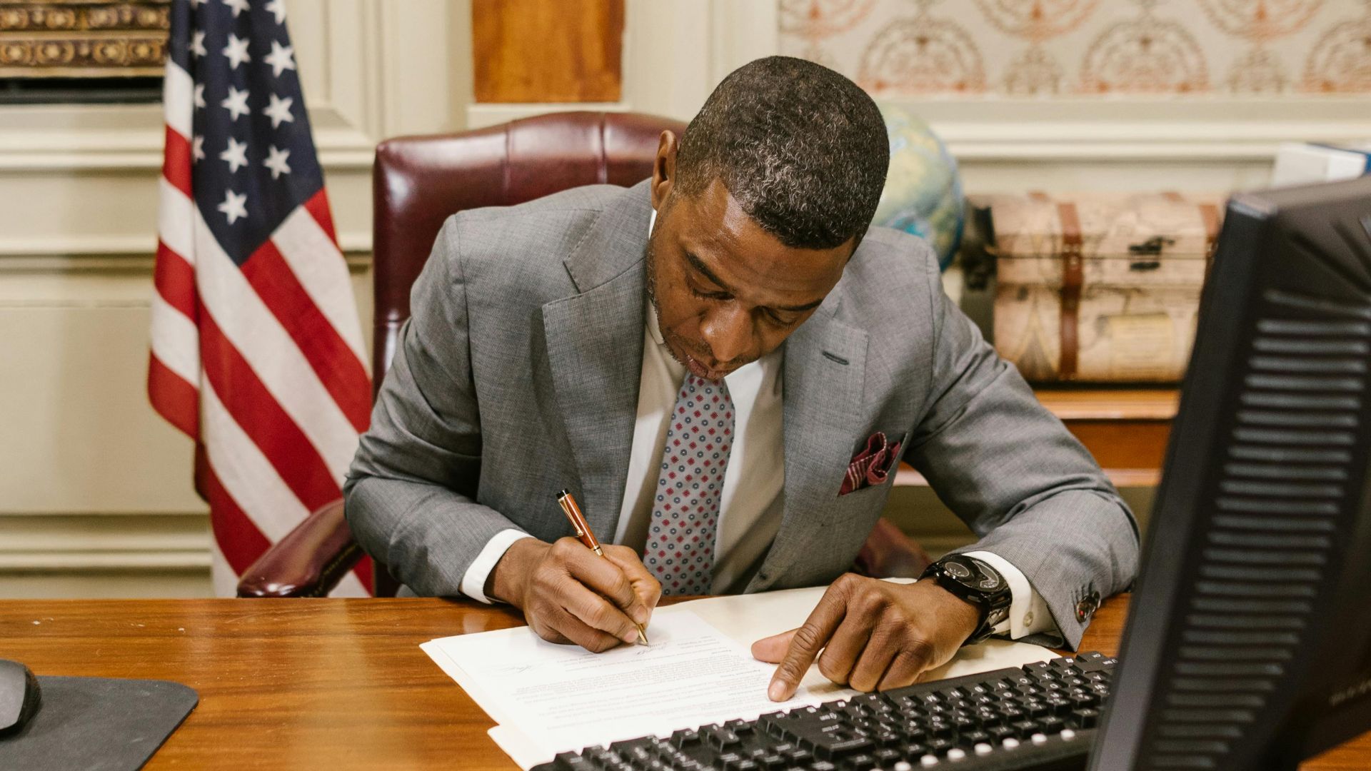 African American lawyer writing documents at a desk in a formal law office.