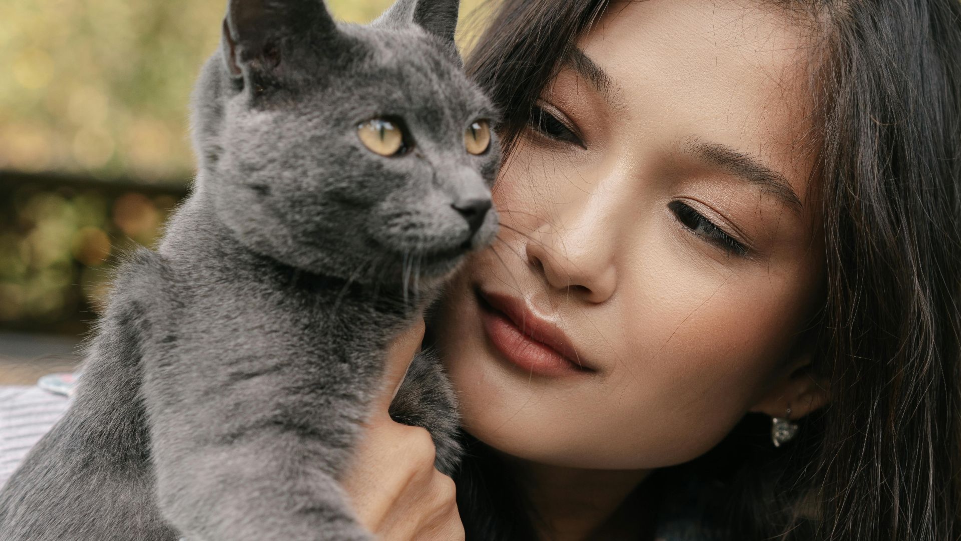 A serene portrait of a young woman lovingly holding a Russian Blue cat in a garden setting.