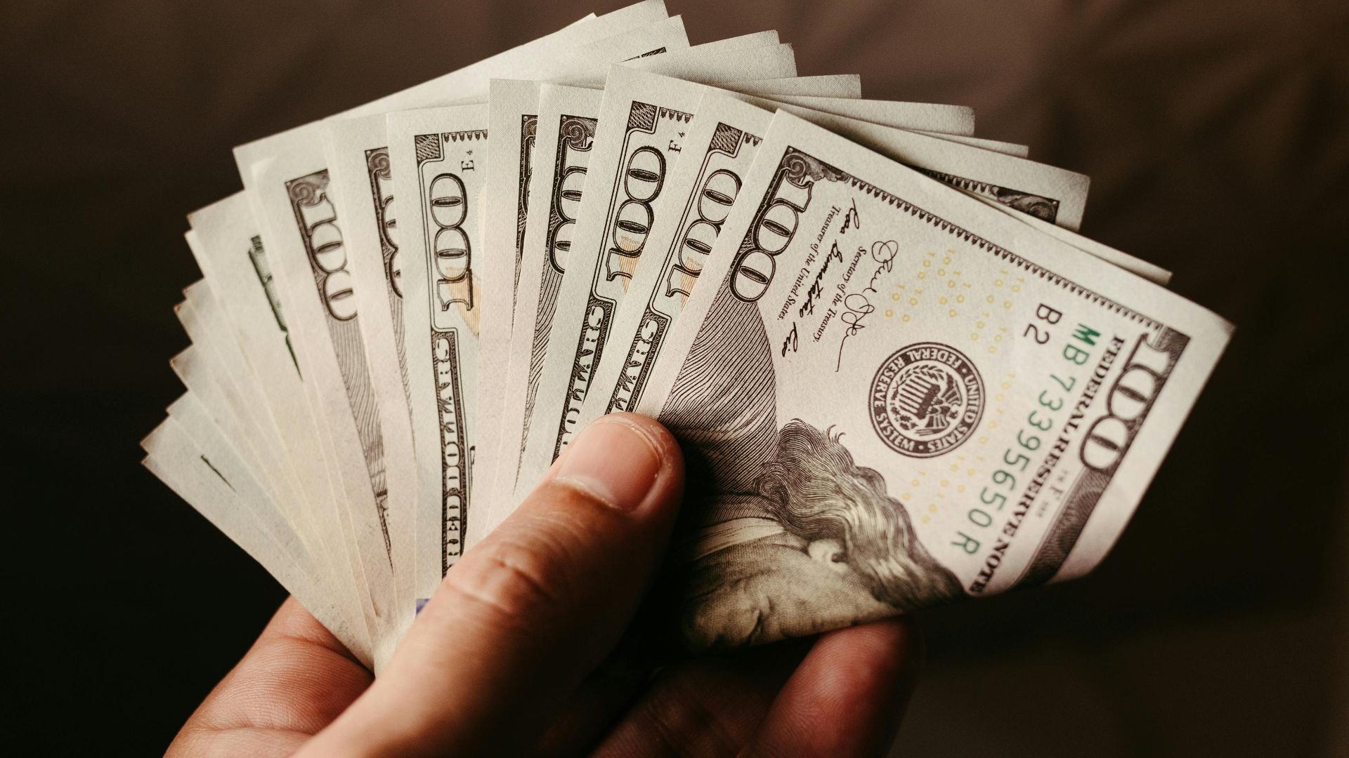Fan of US hundred dollar bills held in hand, symbolizing wealth and finance.