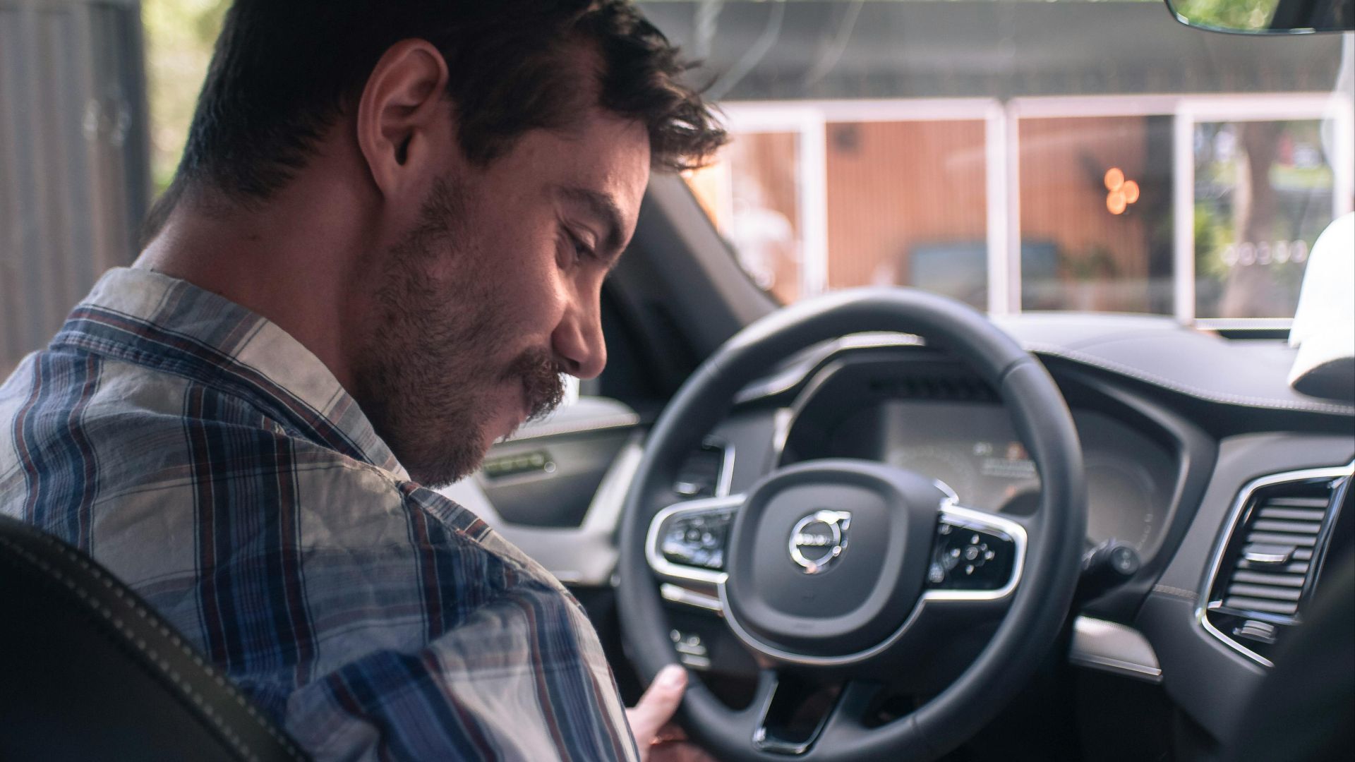 Casually dressed man smiling in the driver seat of a modern Volvo XC90 car interior.