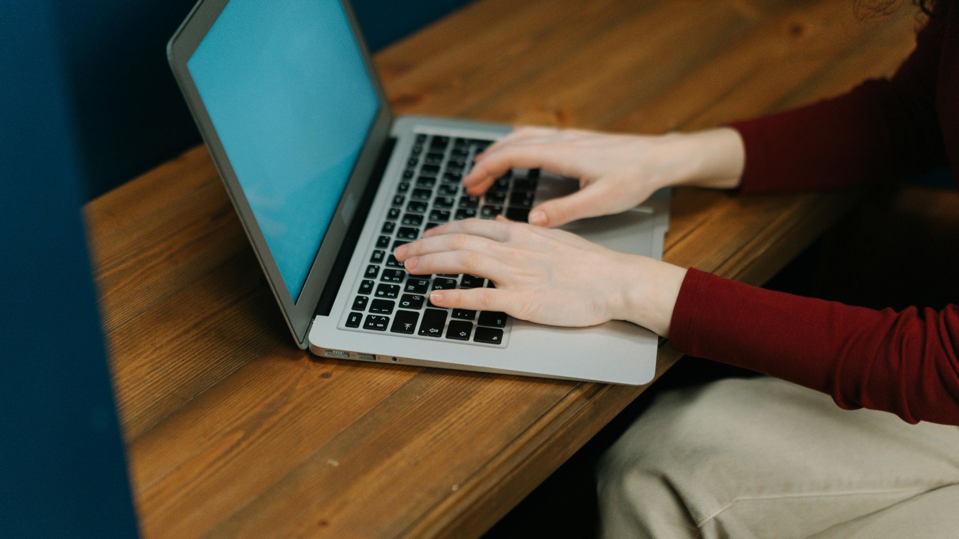 Close-up of a woman typing on a laptop positioned on a wooden table, focused workspace environment.