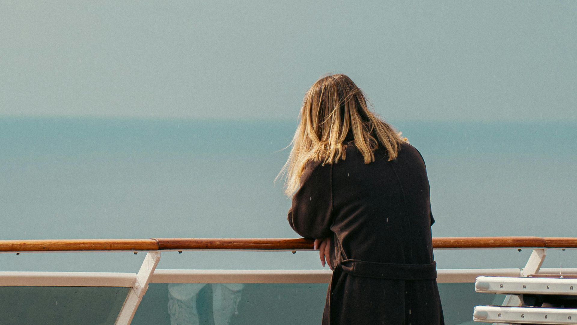 A woman stands on a cruise ship deck gazing at the tranquil sea in Naples, Italy.