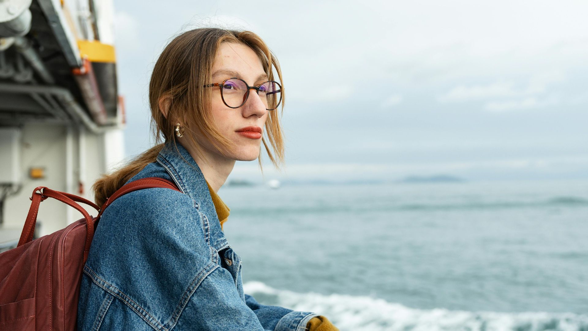 A woman with a backpack gazes at the ocean from a cruise ship deck, capturing a serene moment at sea.