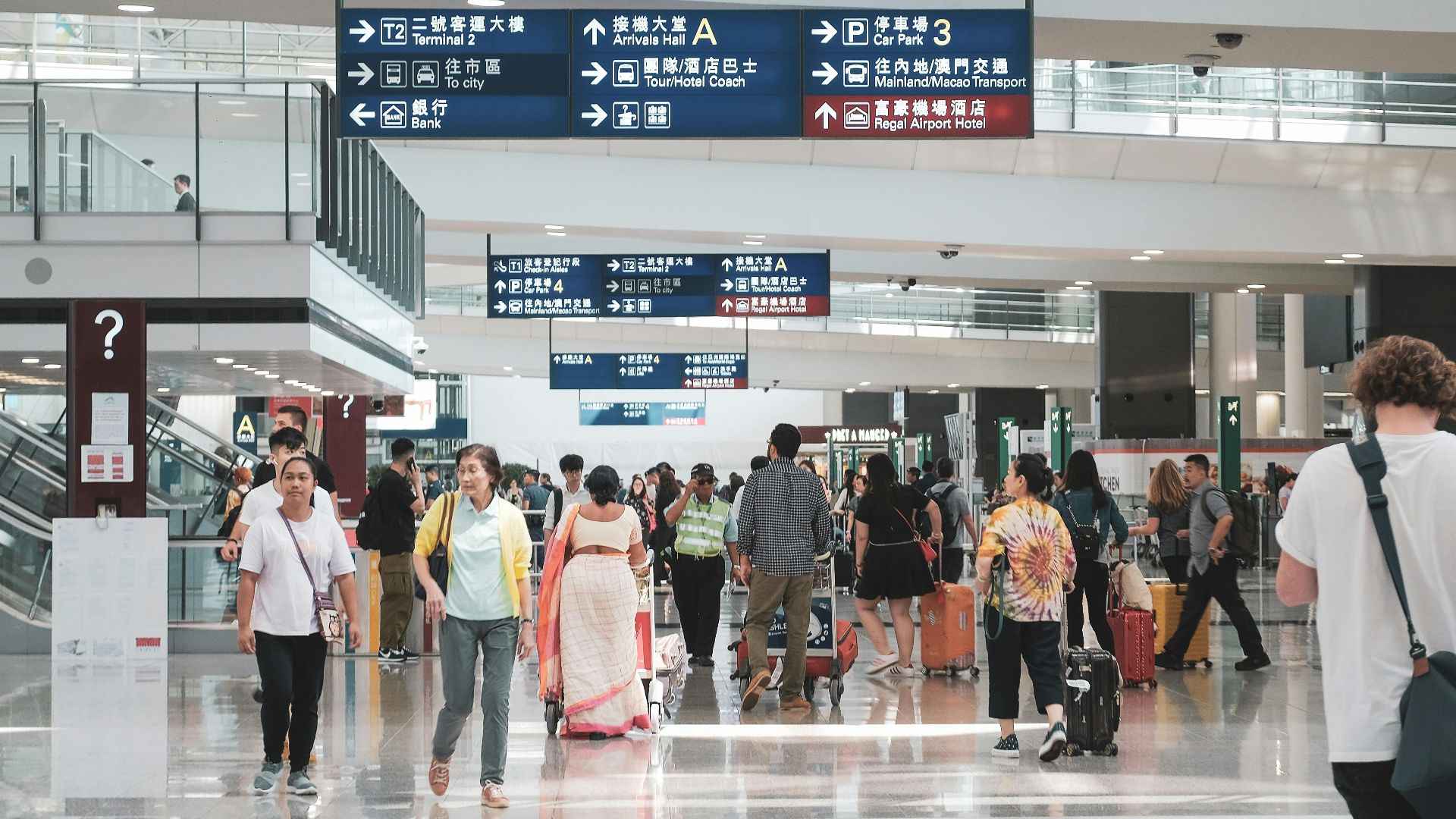 Crowded Hong Kong airport terminal with diverse passengers and informative signage.