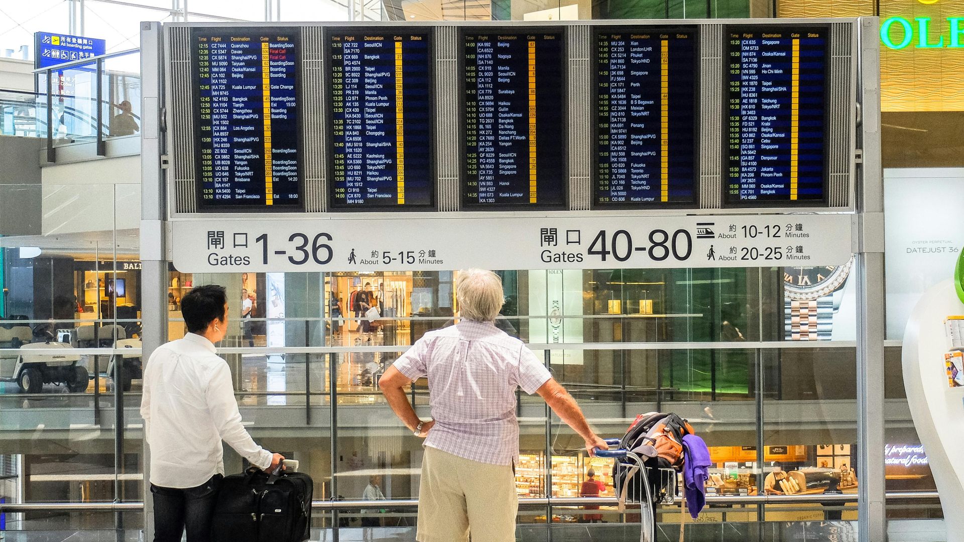 Passengers review flight information on a digital board in Hong Kong airport terminal.