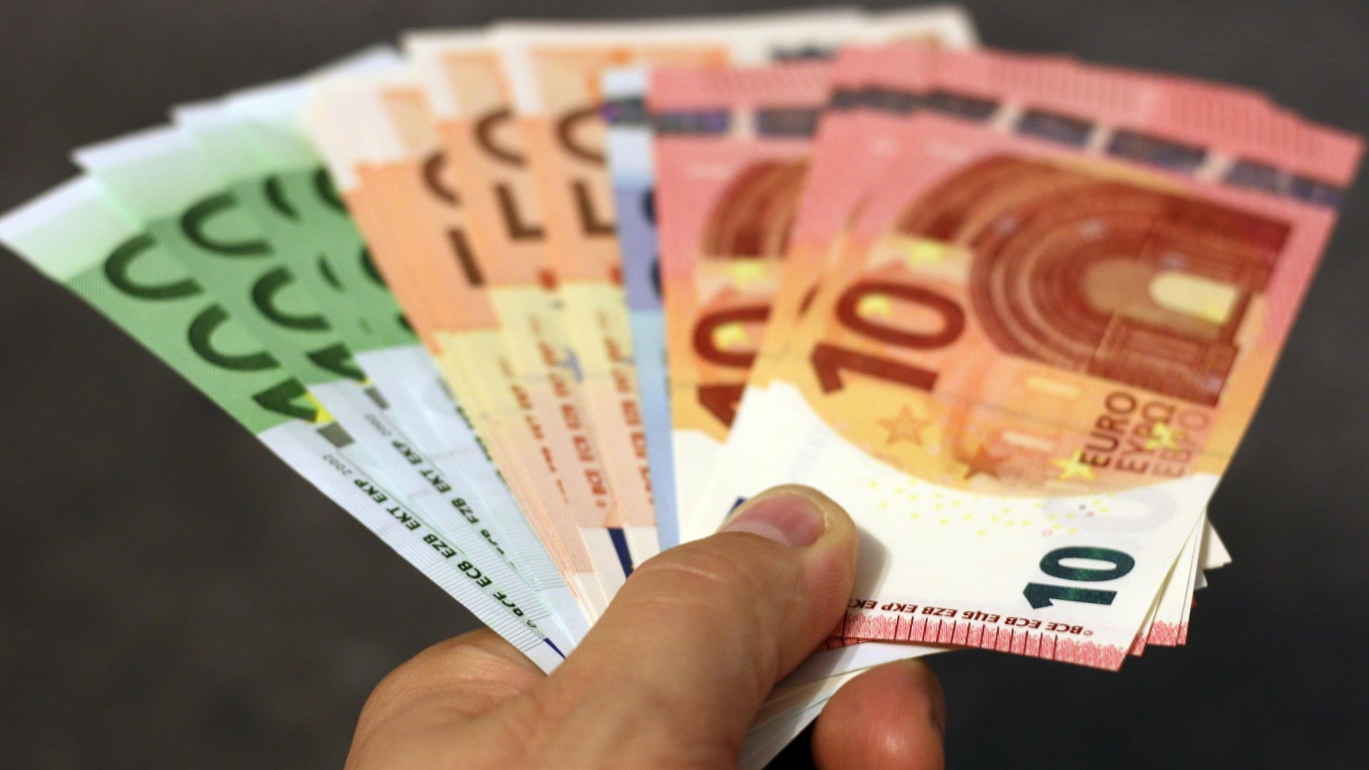 A fan of euro banknotes in various denominations held in a hand.