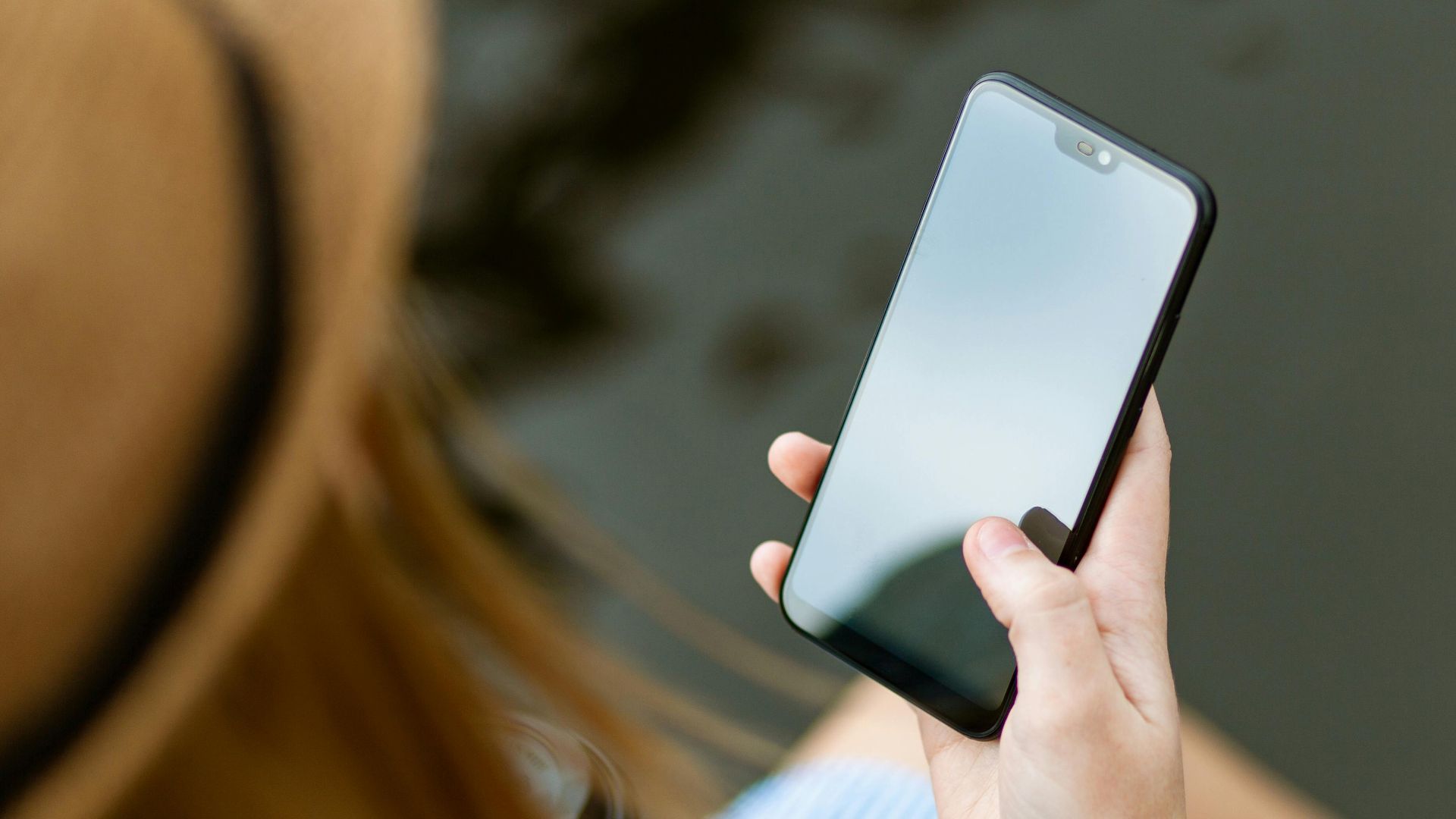 A young woman holding a smartphone while sitting outdoors in summer, capturing a moment of relaxation and technology use.