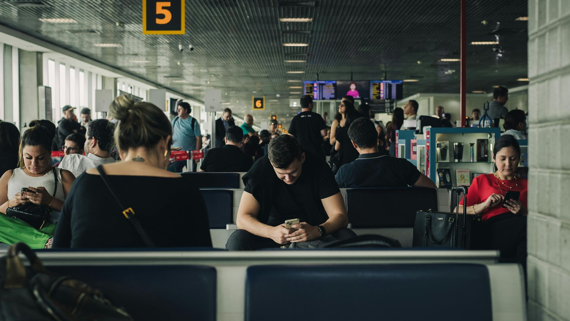 Travelers seated and waiting at São Paulo airport terminal, engaging with smartphones.