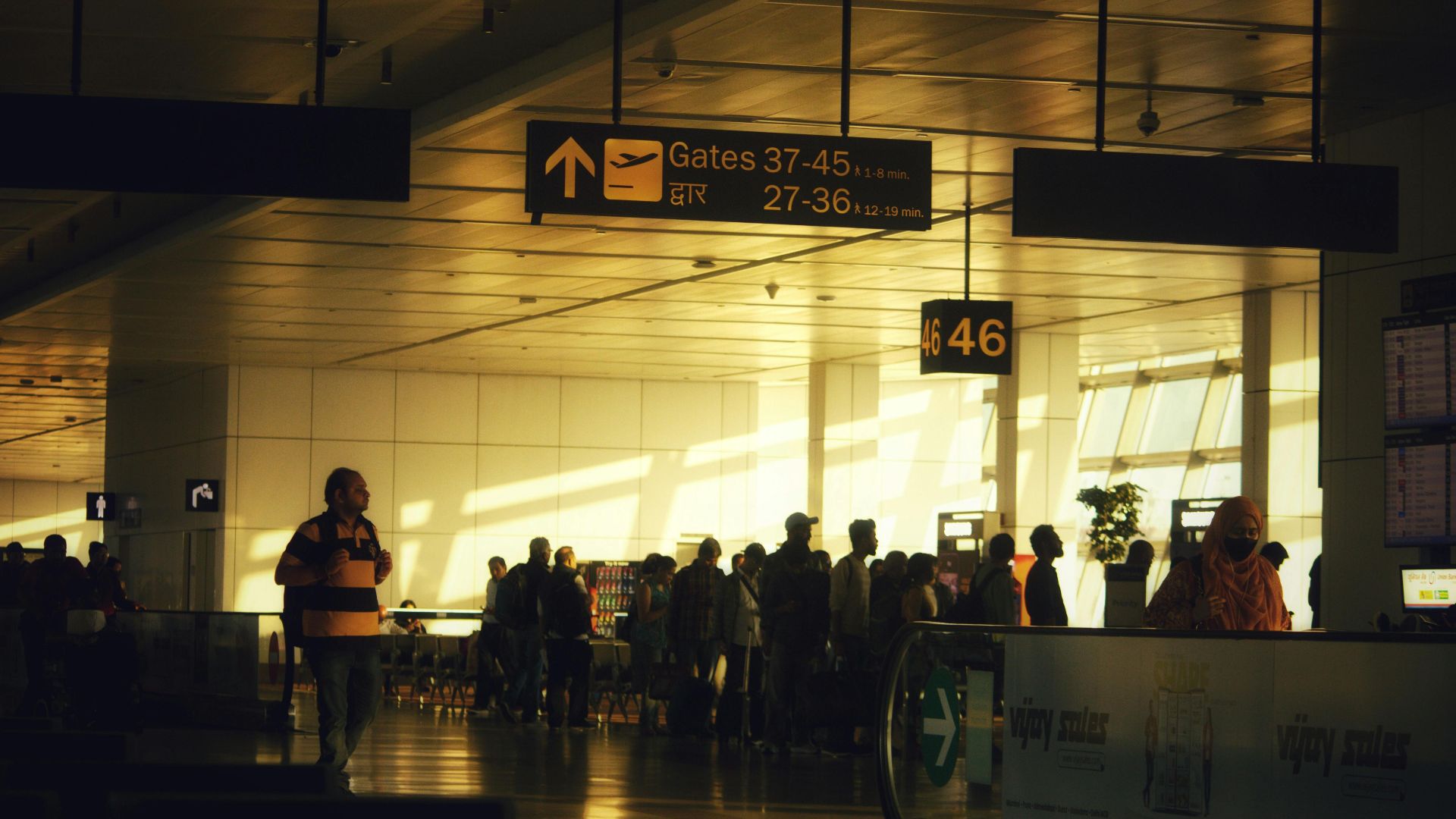 Crowded hallways and directional signs guide travelers in Delhi Airport.