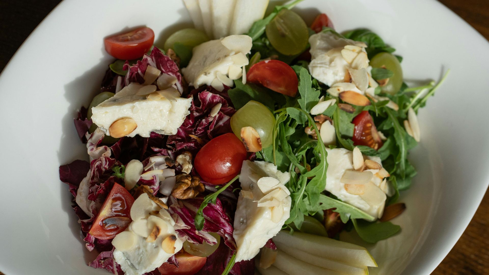 Colorful salad with brie cheese, grapes, and almonds on a white plate.