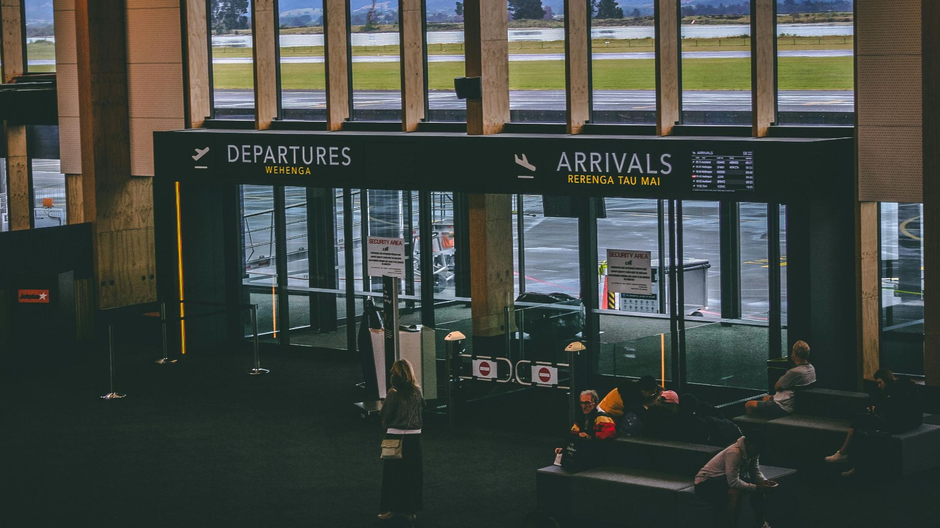 Busy airport terminal area with people, featuring departures and arrivals signs.