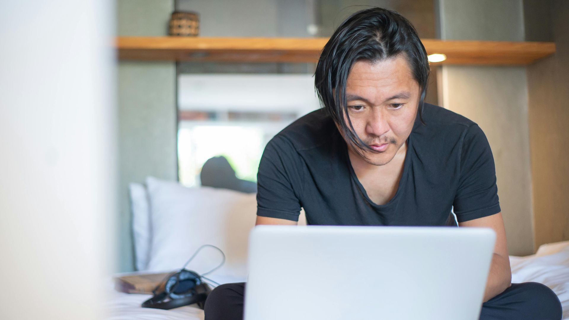 An Asian man working from home on a laptop, focusing on his digital tasks in a cozy indoor setting.