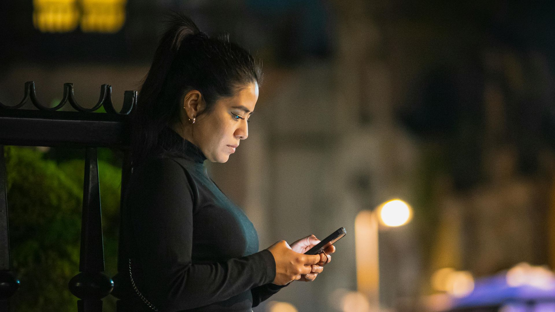 A woman is engrossed in her smartphone on a bustling street in Mexico City at night.